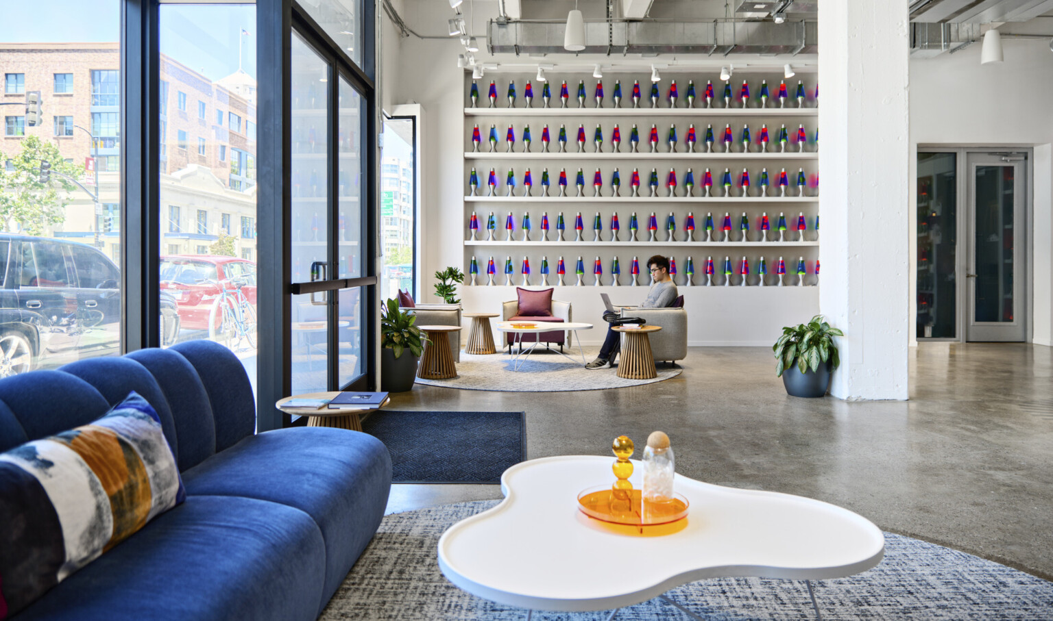 Cloudflare San Francisco Headquarters lobby with mixed comfortable seating and tall ceilings. Wall of blue and pink lava lamps on white built in shelves