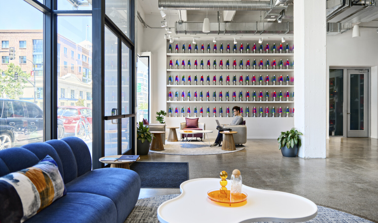 Cloudflare San Francisco Headquarters lobby with mixed comfortable seating and tall ceilings. Wall of blue and pink lava lamps on white built in shelves