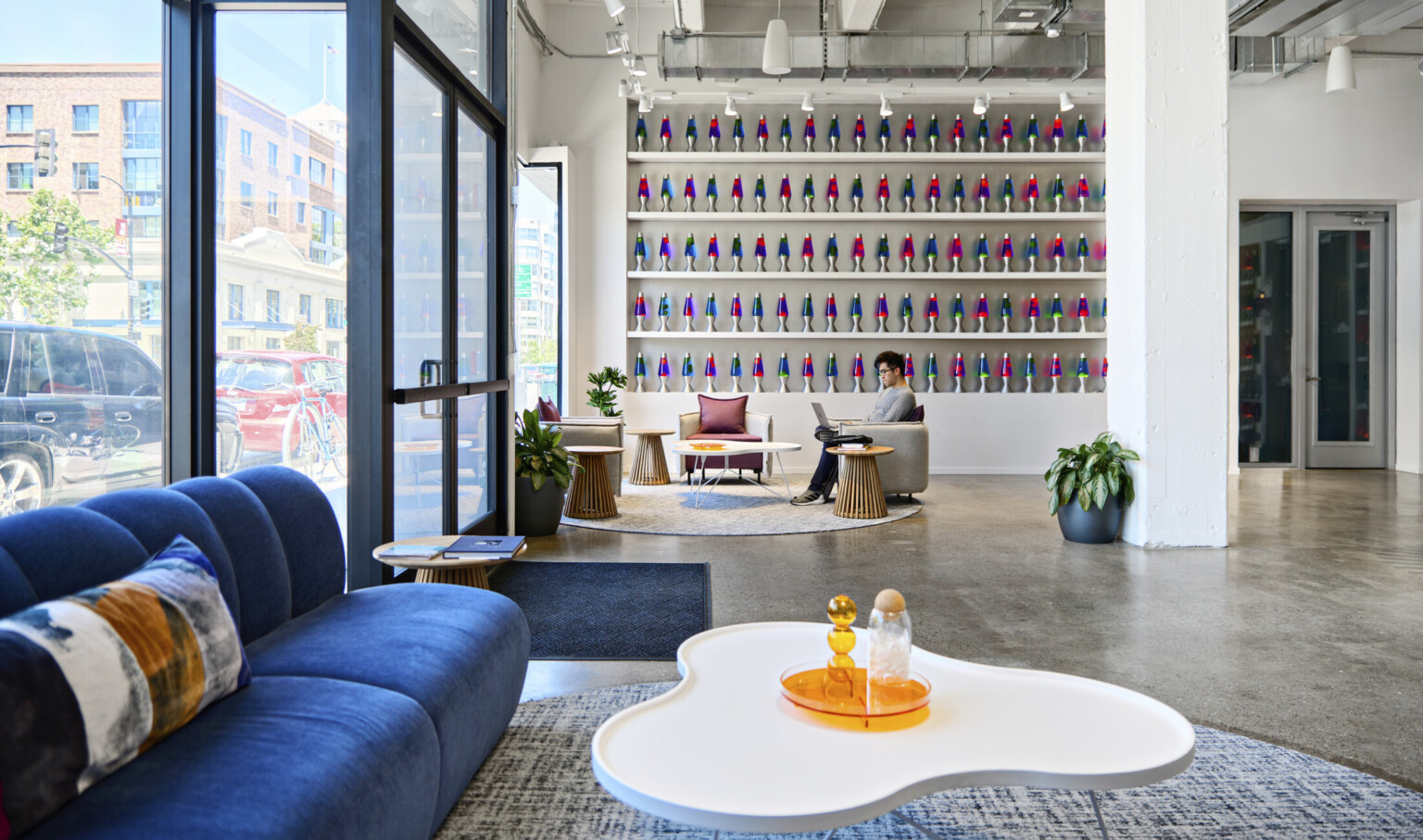 Cloudflare San Francisco Headquarters lobby with mixed comfortable seating and tall ceilings. Wall of blue and pink lava lamps on white built in shelves
