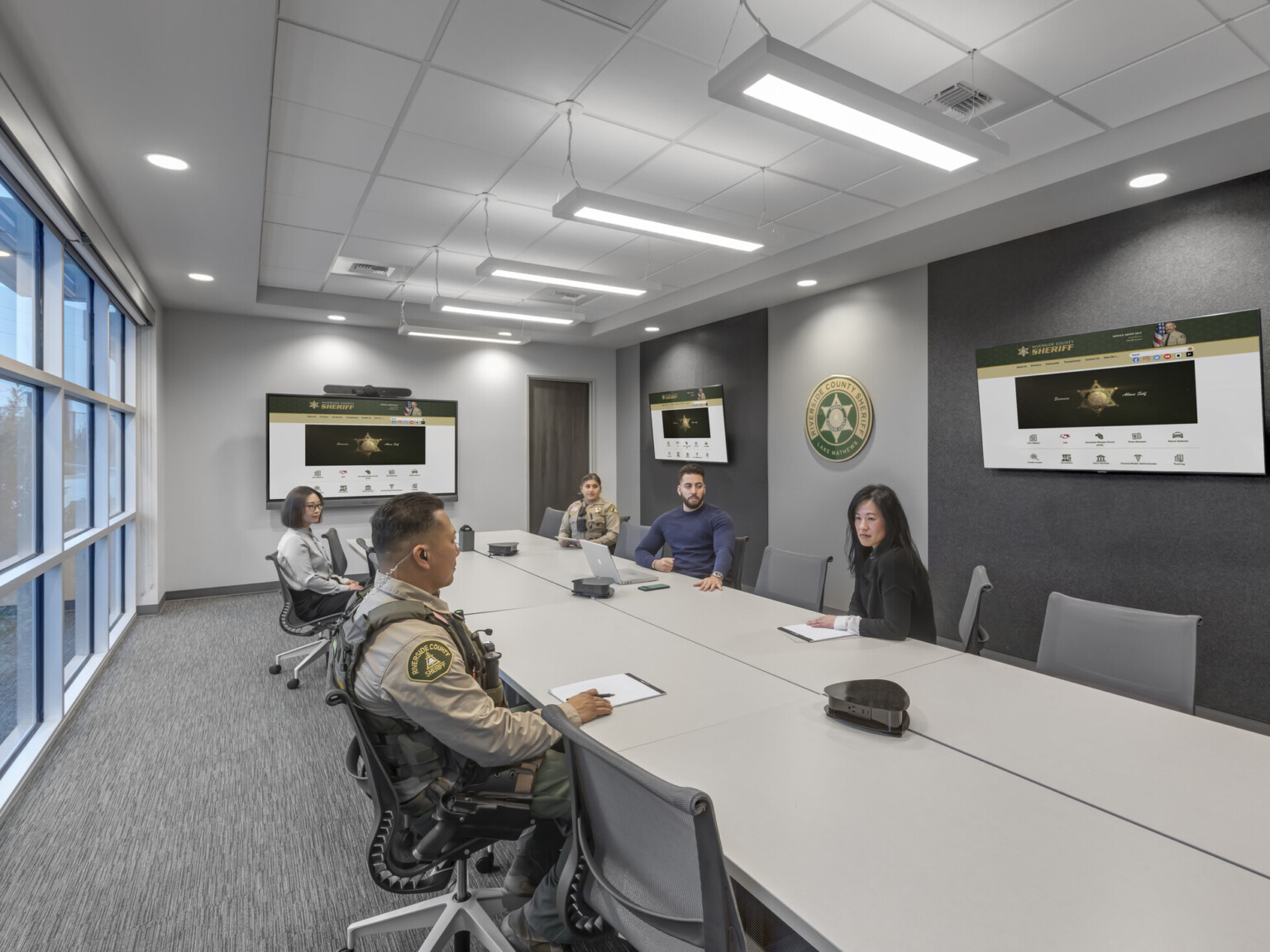 several officers and employees seated in conference room with video and remote meeting capabilities, soundproofing, floor-to-ceiling windows, natural light fixtures