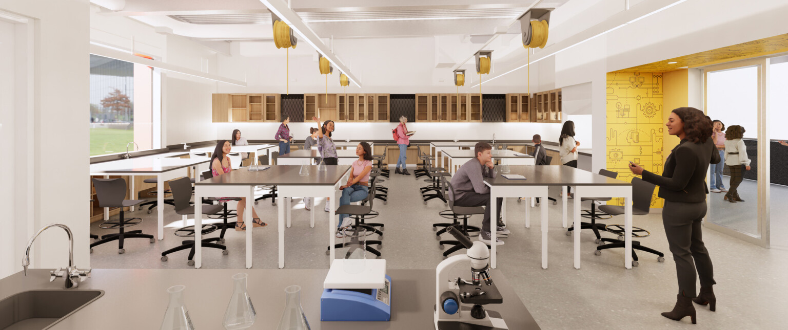 Classroom lab with yellow accents, yellow cables suspended from the ceiling, high tables, and students interacting with their teacher