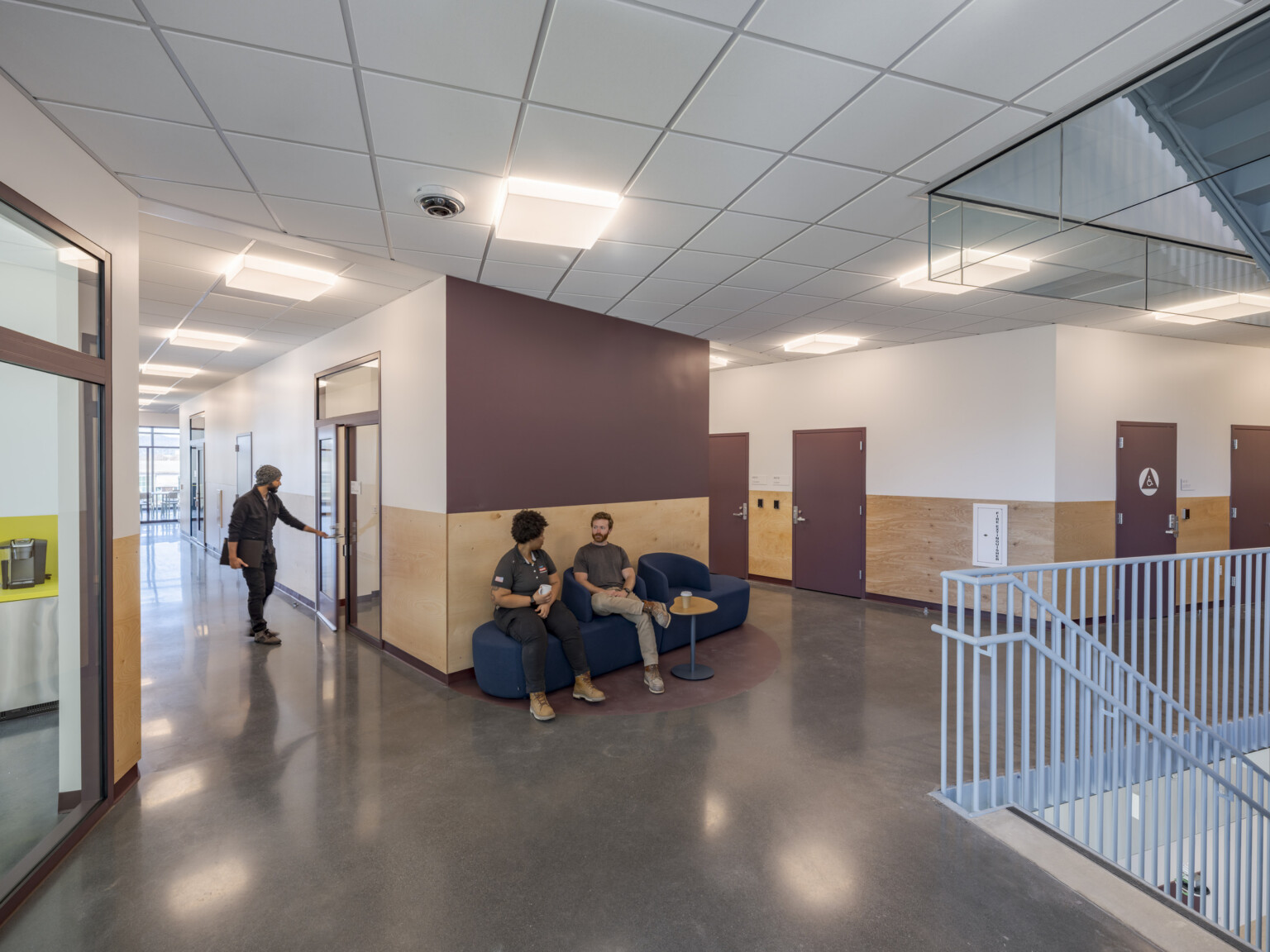 People converse in a comfortable seating area at the top of a staircase, surrounded by hallways, doors, and windows.