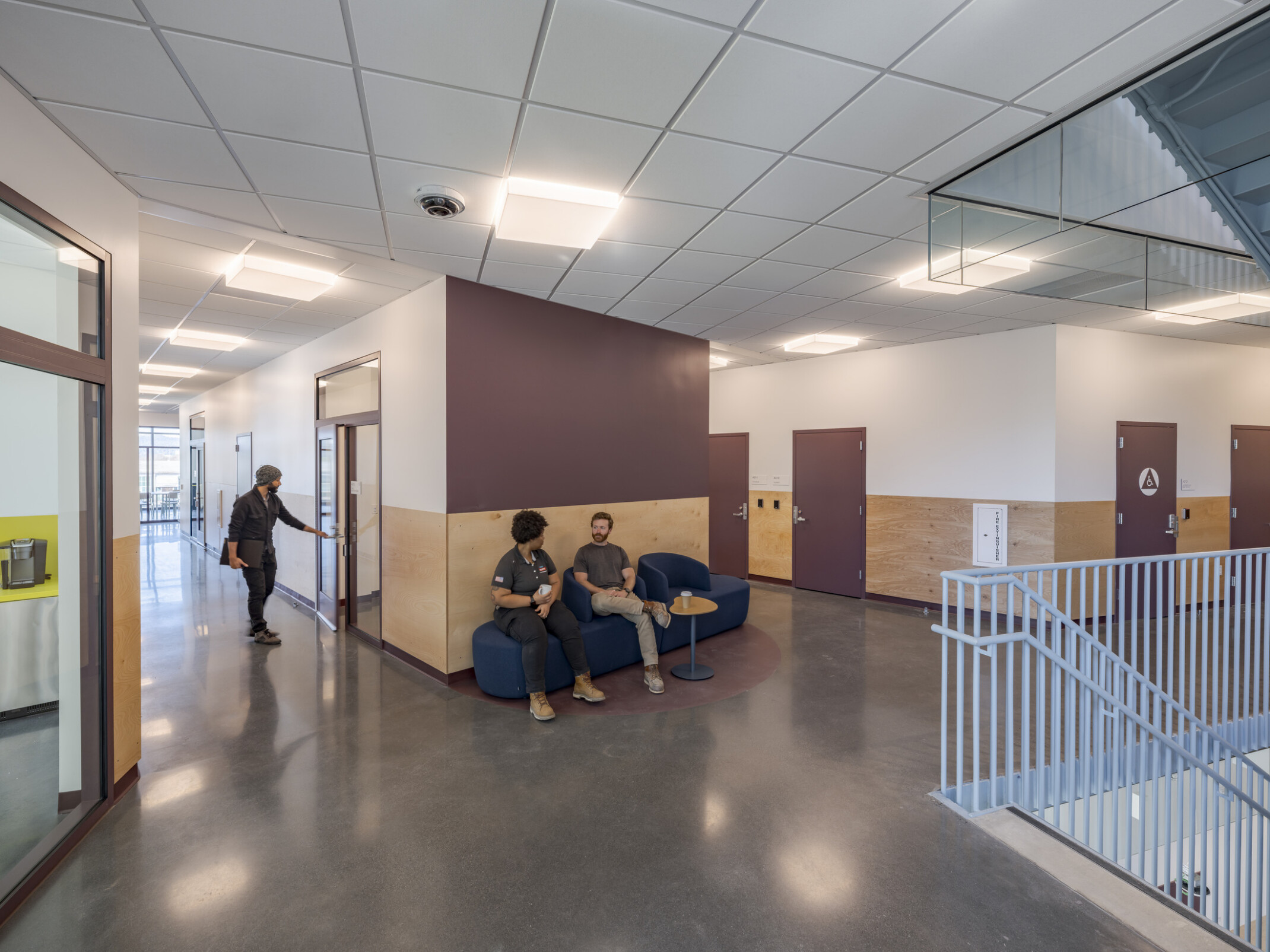 People converse in a comfortable seating area at the top of a staircase, surrounded by hallways, doors, and windows.