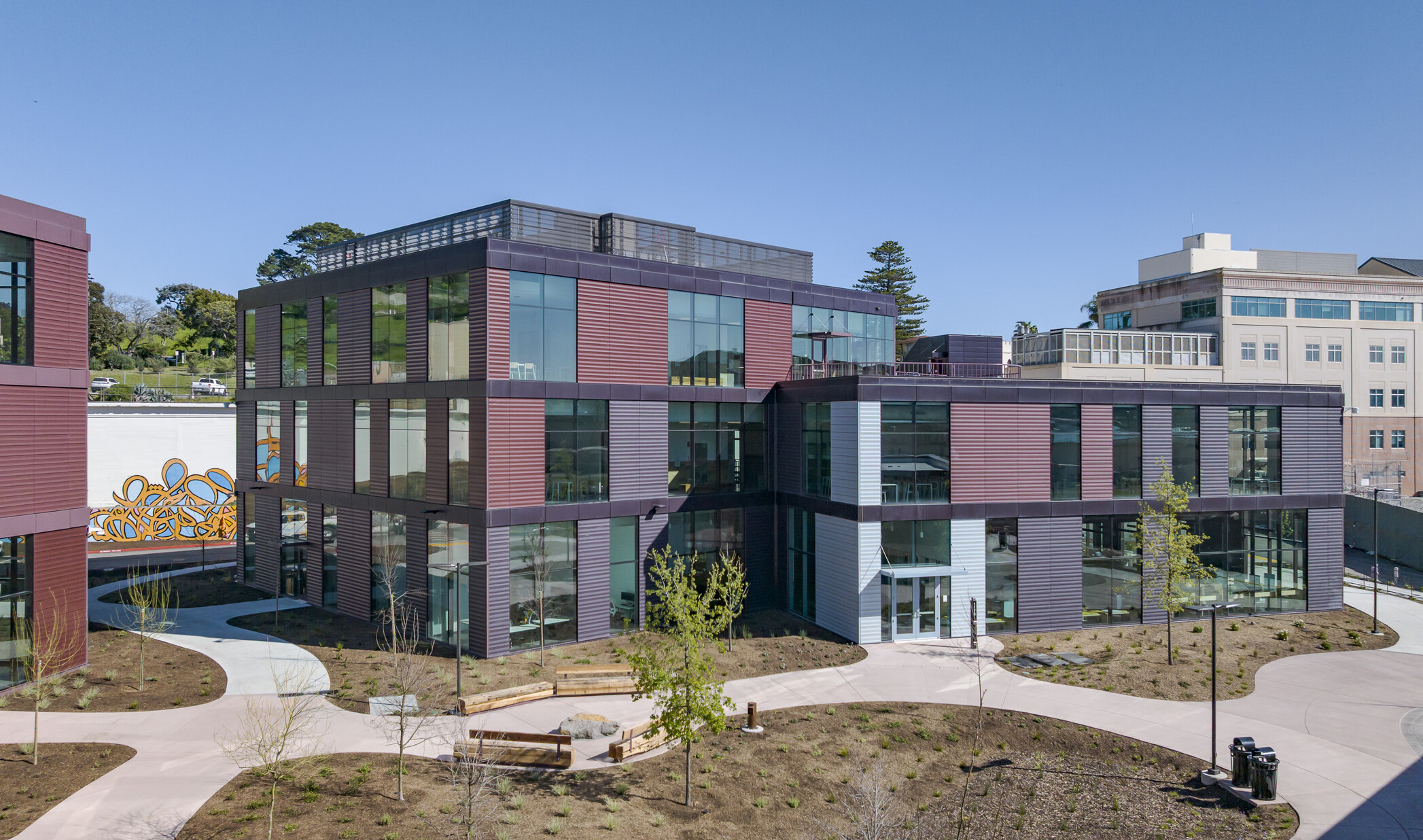 One of the new center buildings features maroon and deep purple paneling, floor-to-ceiling windows, and open walkways with wooden benches that lead into the central courtyard.