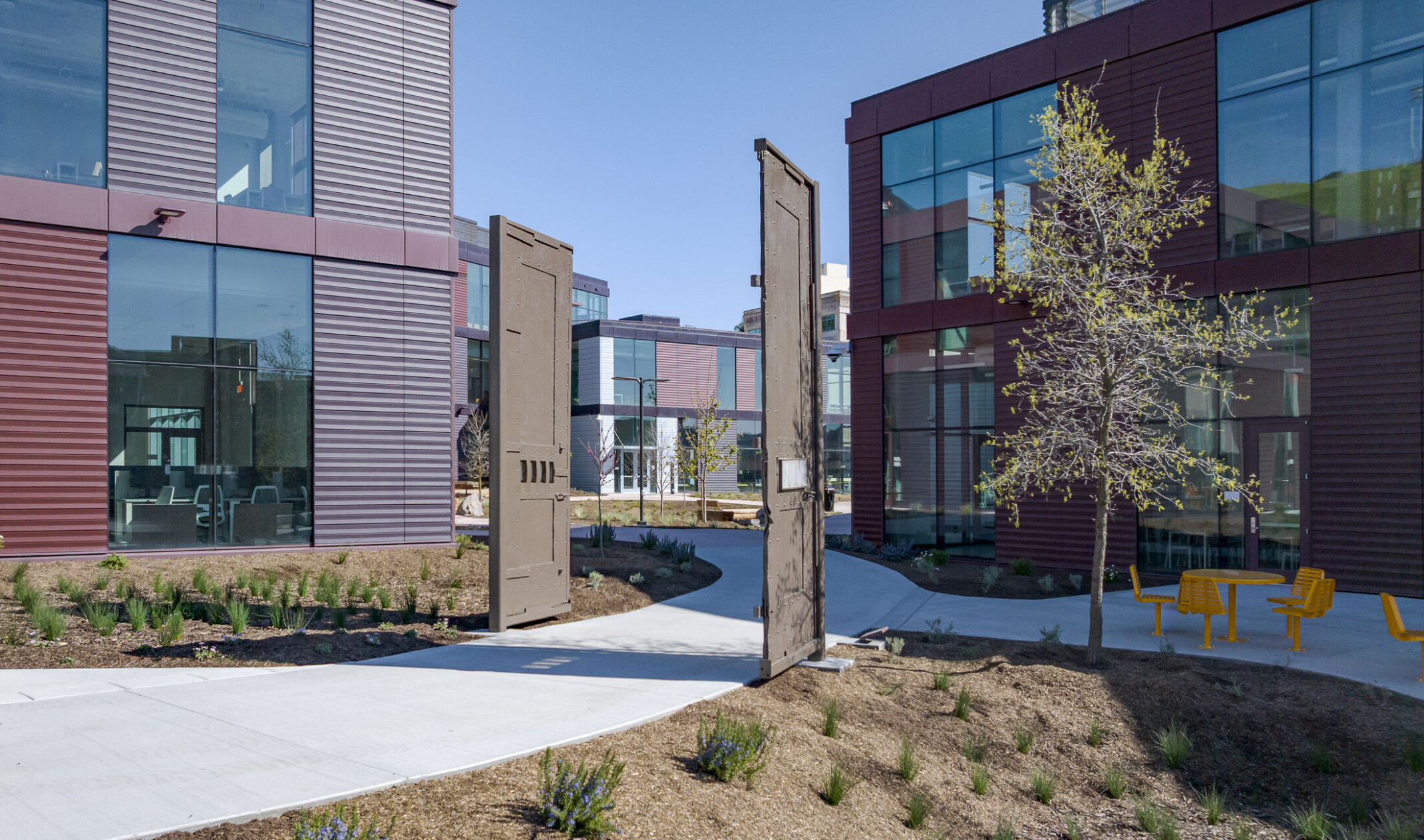 Courtyard walkways connecting the facility’s buildings, featuring natural landscaping, wide paths, and standalone gates on either side of a central walkway as a nod to the previous structure.