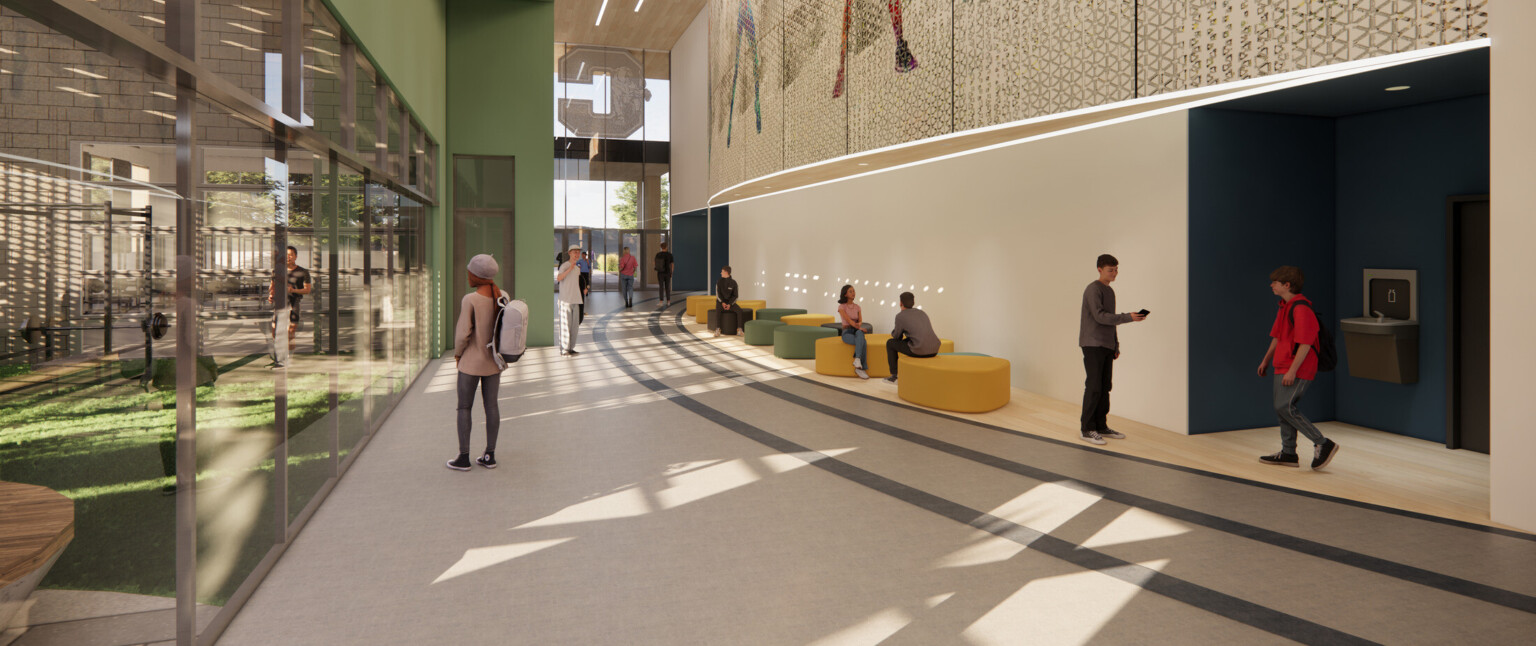 Curved hallway in a building with large glass windows and students lounging on green and yellow couches
