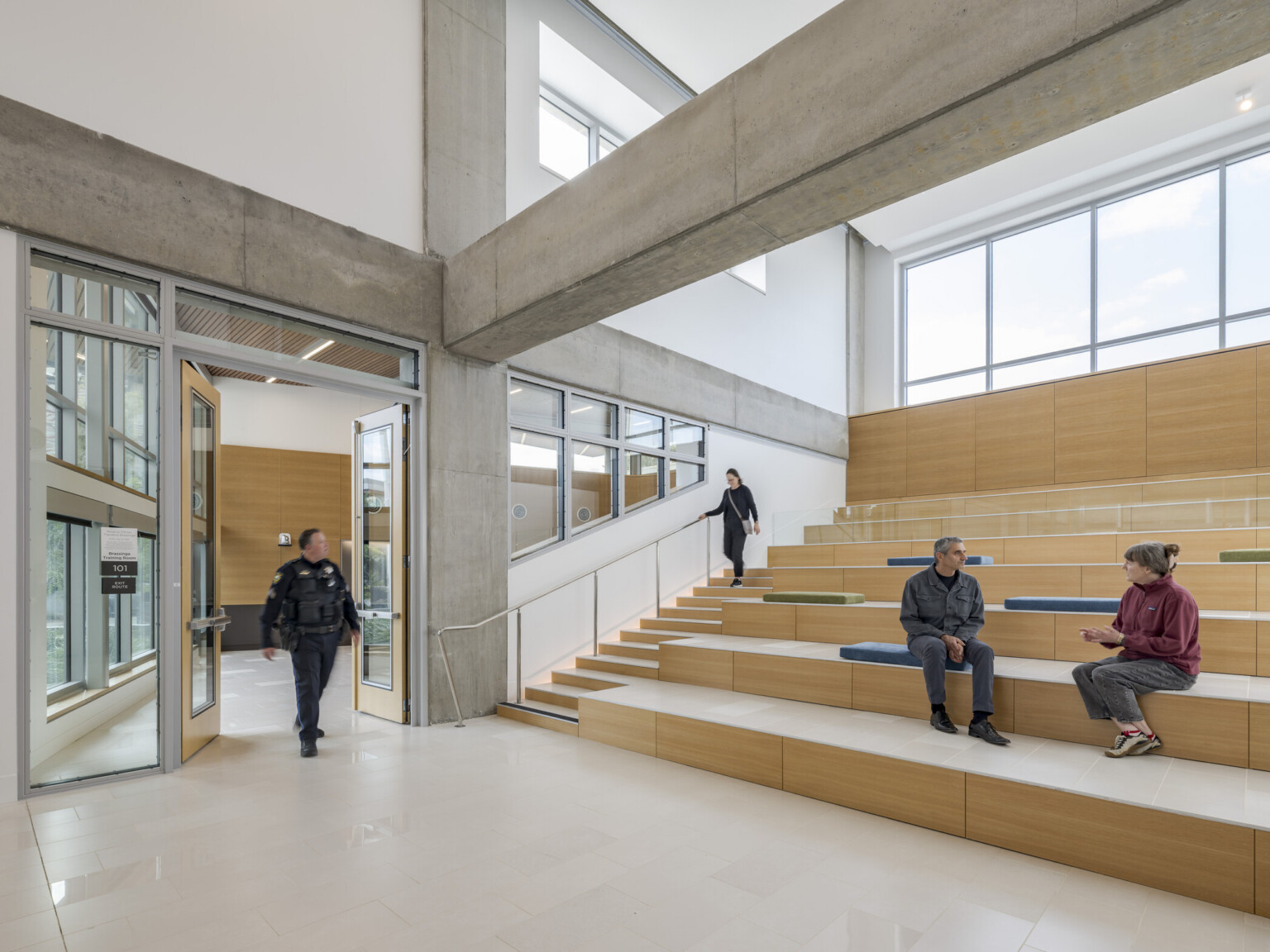 Palo Alto Public Safety Building & Emergency Operations Center; Detectives in suits and uniformed police officers sit in conversation at café tables and soft seating in a double-height atrium