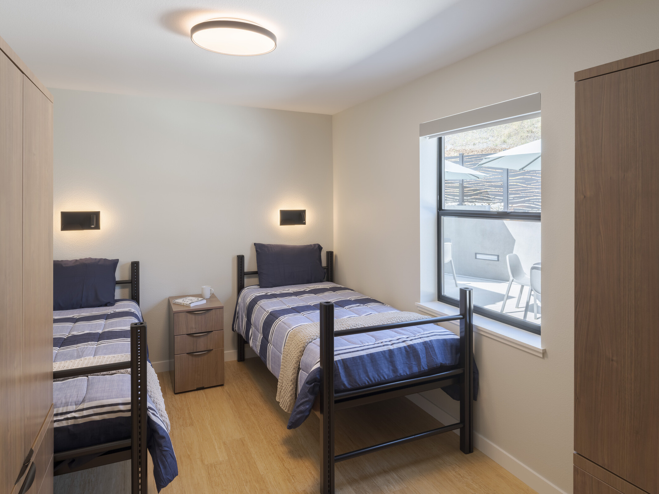 Residential room with two beds and a large window filling the space with natural light.