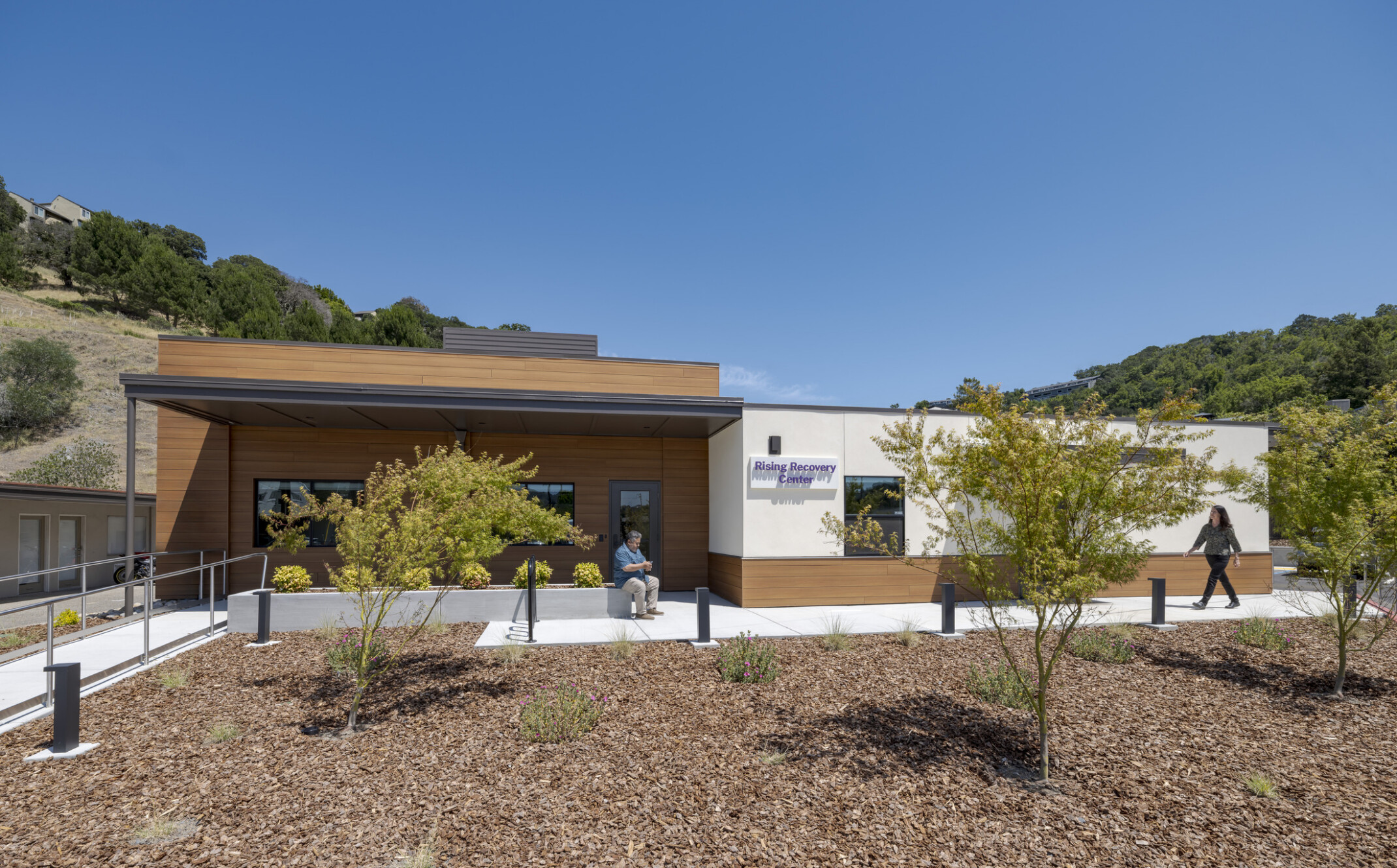 Wide exterior view of the white facade entrance featuring wood accents with neat landscaping, young native trees.