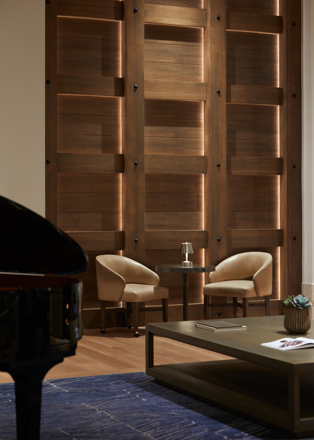 Elegant conversation area with tan leather chairs and a coffee table in front of a backlit wooden wall