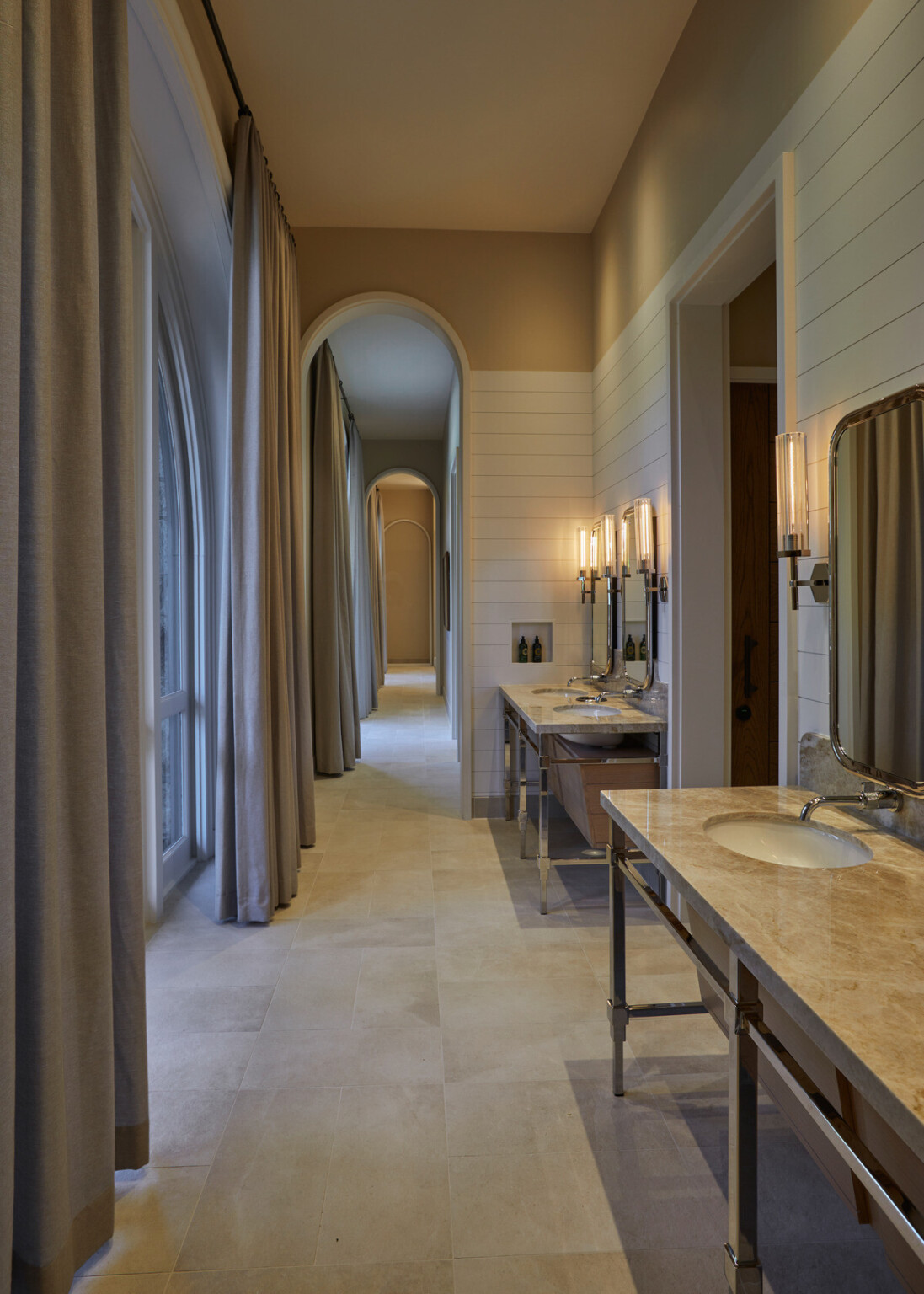 Elegant bathroom hallway with arched windows opposite counters with sinks and mirrors and lighting above