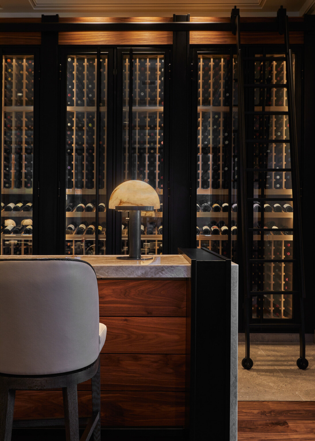 Wine cellar with glass-enclosed wine racks and a marble-topped wooden counter with a lamp