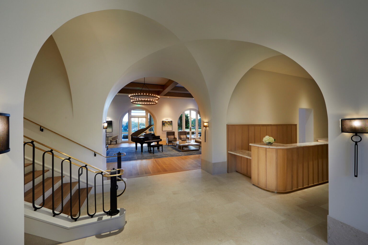 Elegant foyer with arches, a staircase, grand piano and desk