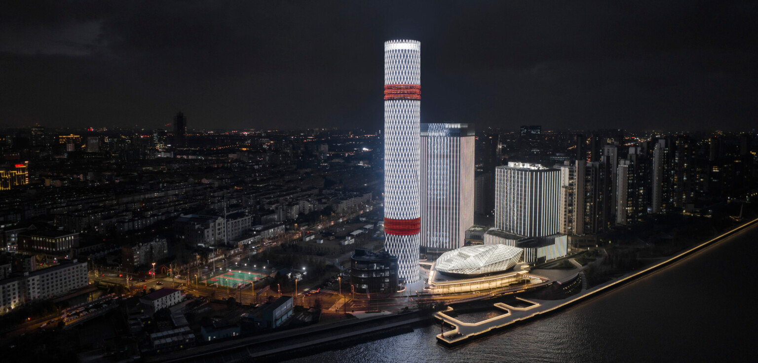 Baoshan Long Beach Complex illuminated at night along Shanghai's Yangtze River, diamond geometric light on cylindrical tower