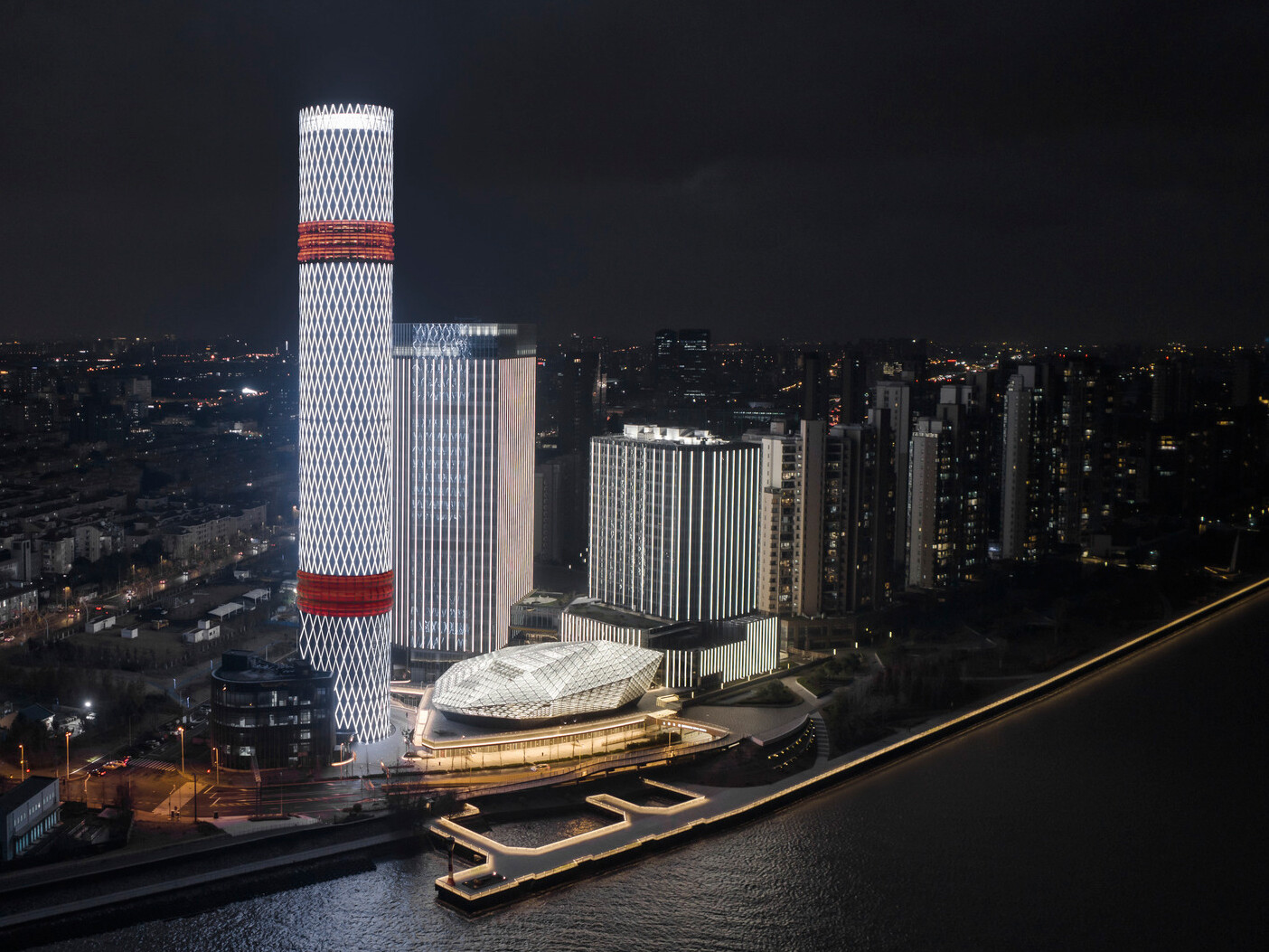 Baoshan Long Beach Complex illuminated at night along Shanghai's Yangtze River, diamond geometric light on cylindrical tower