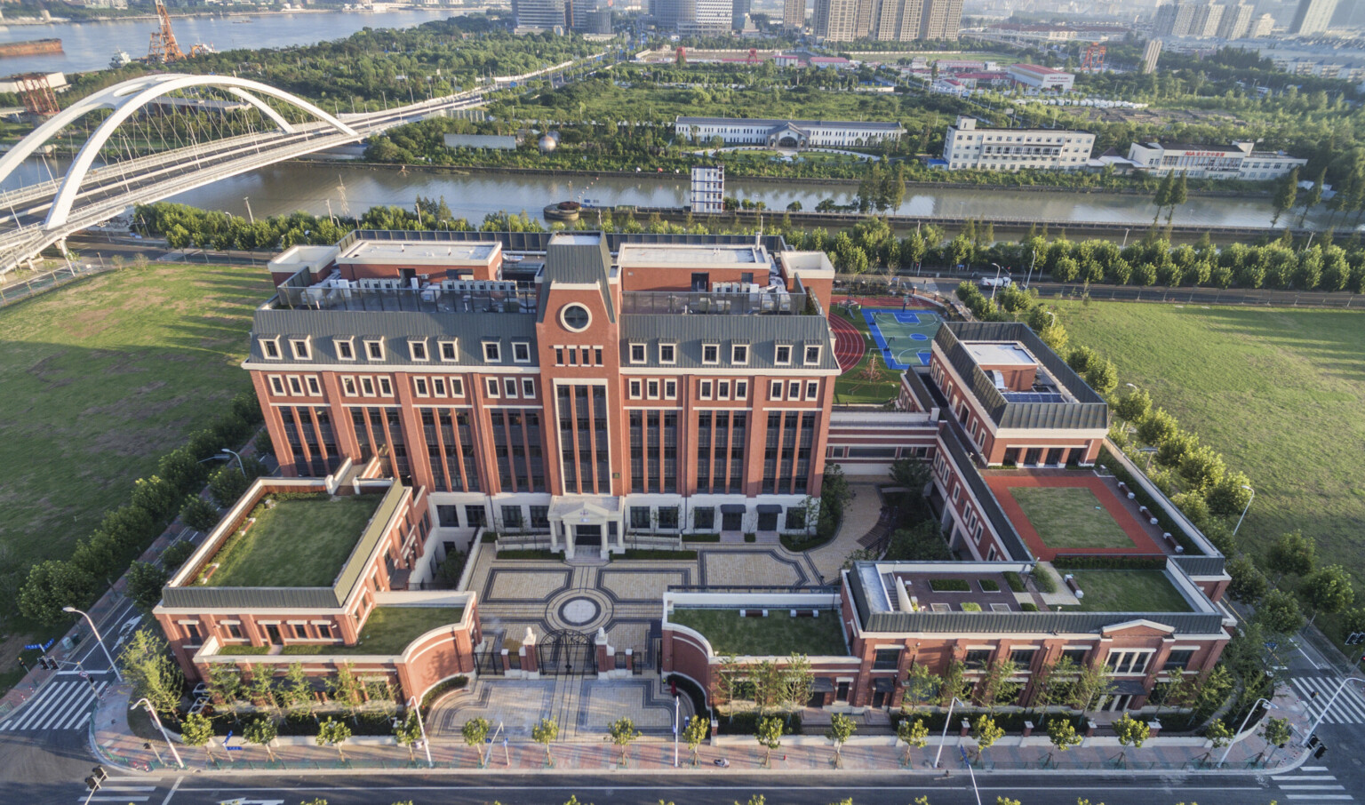 Aerial view of Huili campus from front. A gated stone courtyard is surrounded by brick buildings with living roof sections Aerial view of Huili campus from front. A gated stone courtyard is surrounded by brick buildings with living roof sections