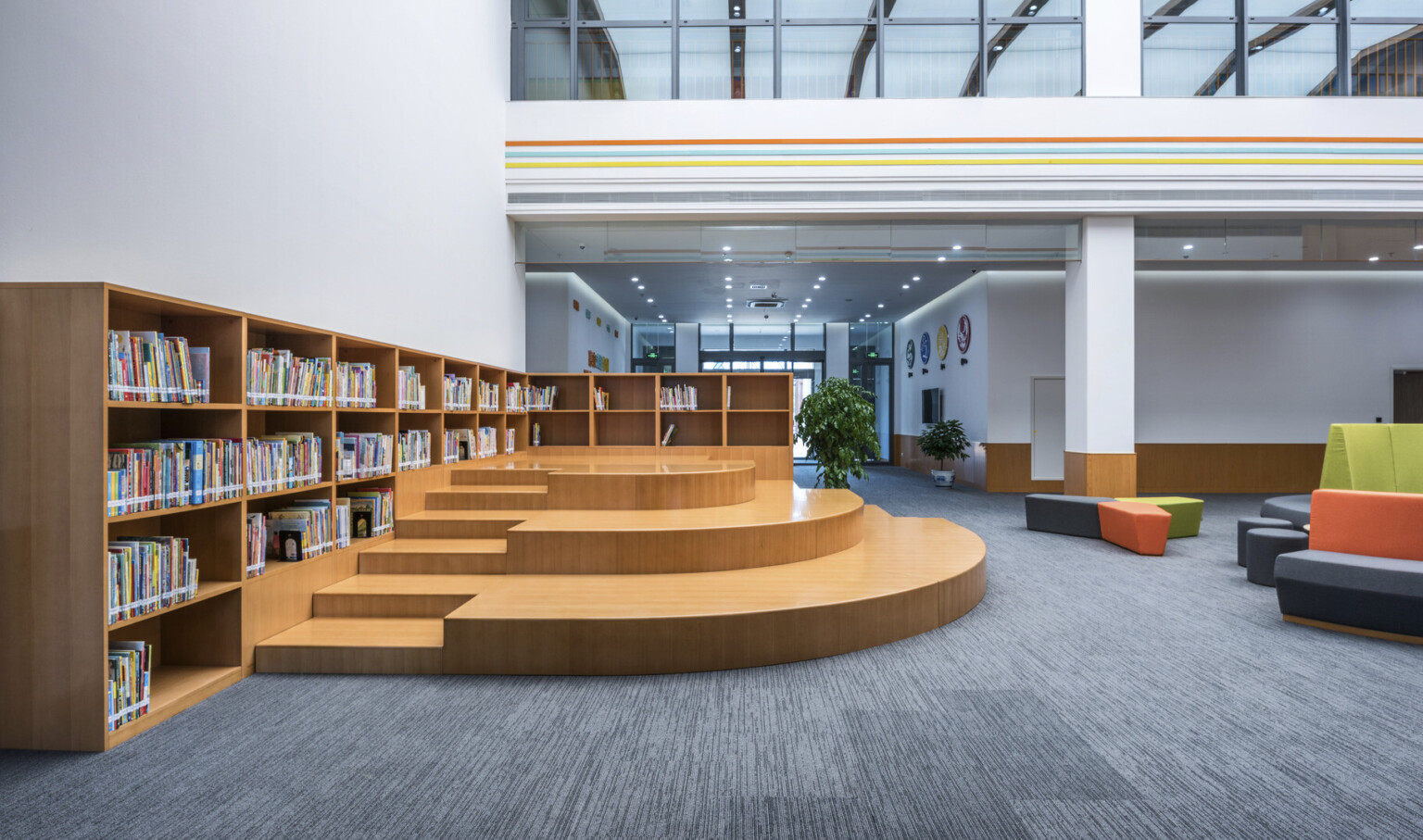 Another view of the atrium with seating to the right. Left, a wood L shaped bookcase lines the wall with stepped seating
