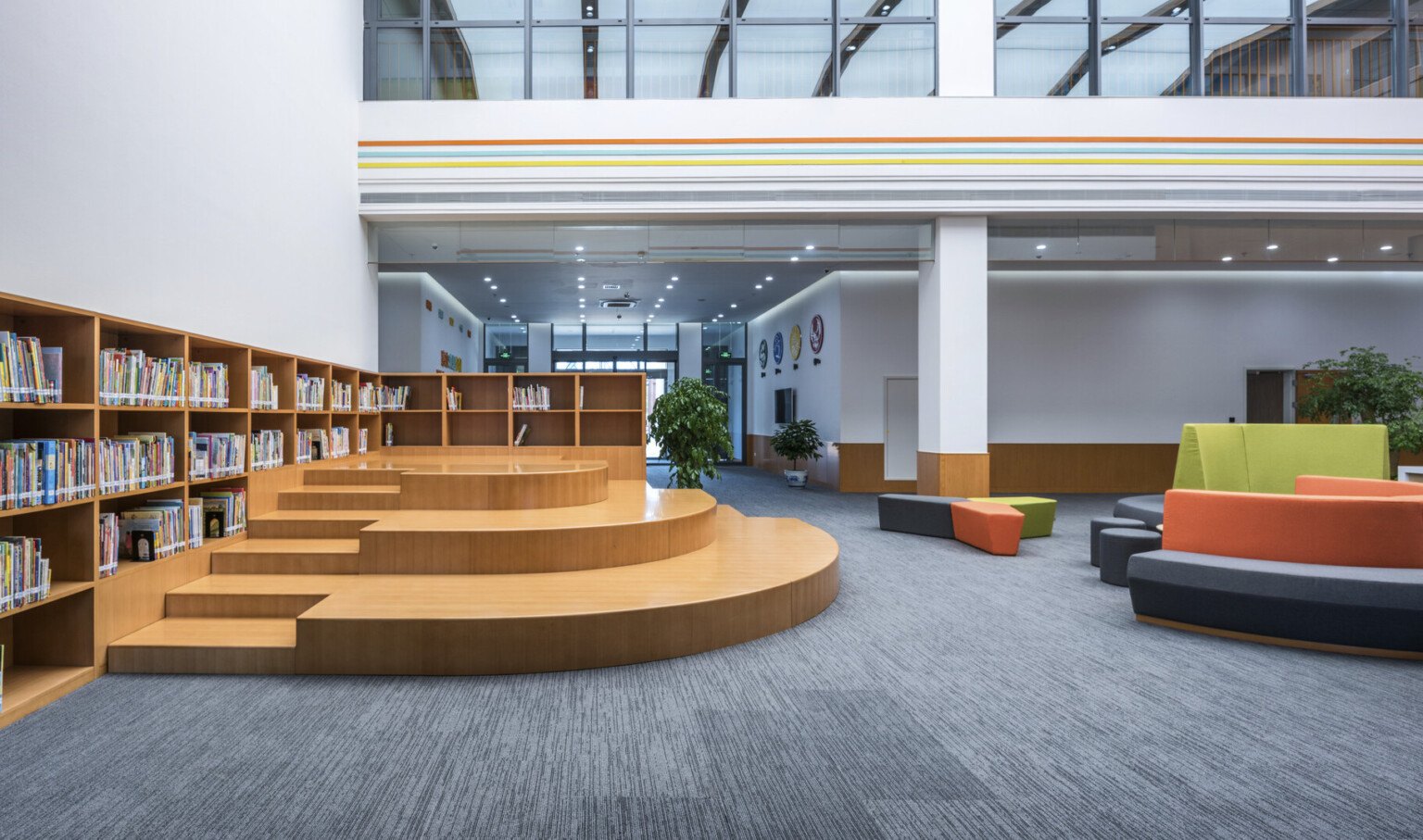 Another view of the atrium with seating to the right. Left, a wood L shaped bookcase lines the wall with stepped seating