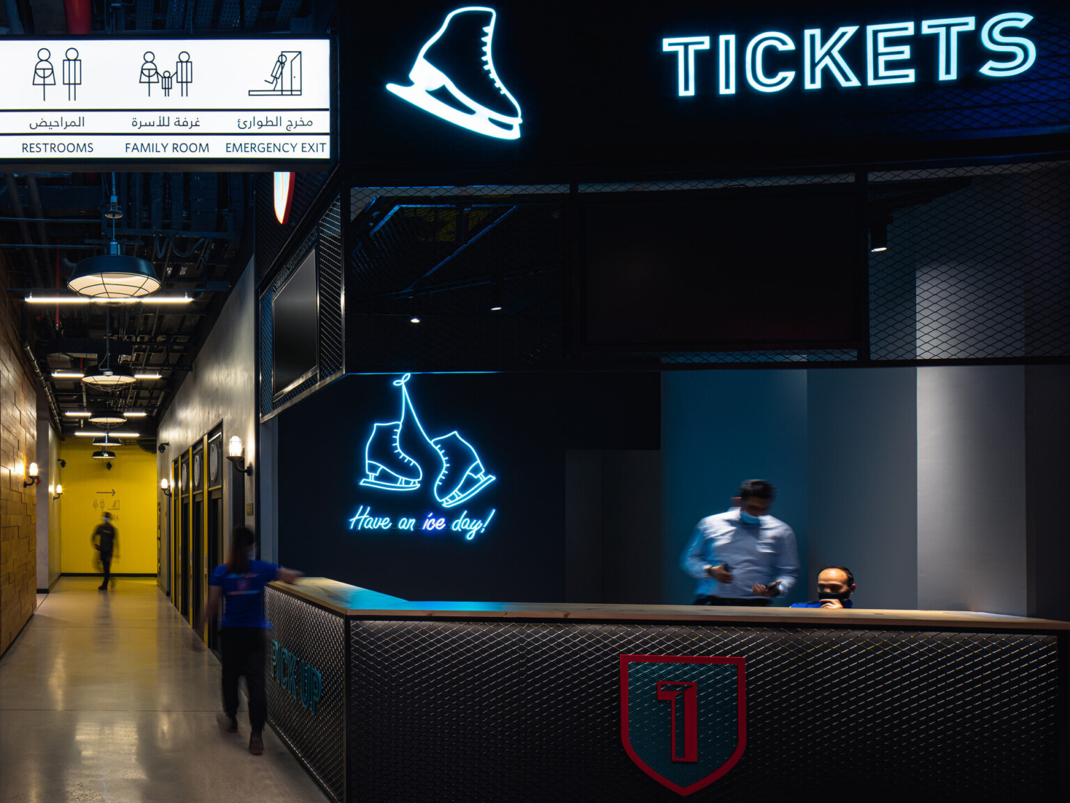 Ticket counter for ice rink with dark walls, directional signage, and blue neon lighting