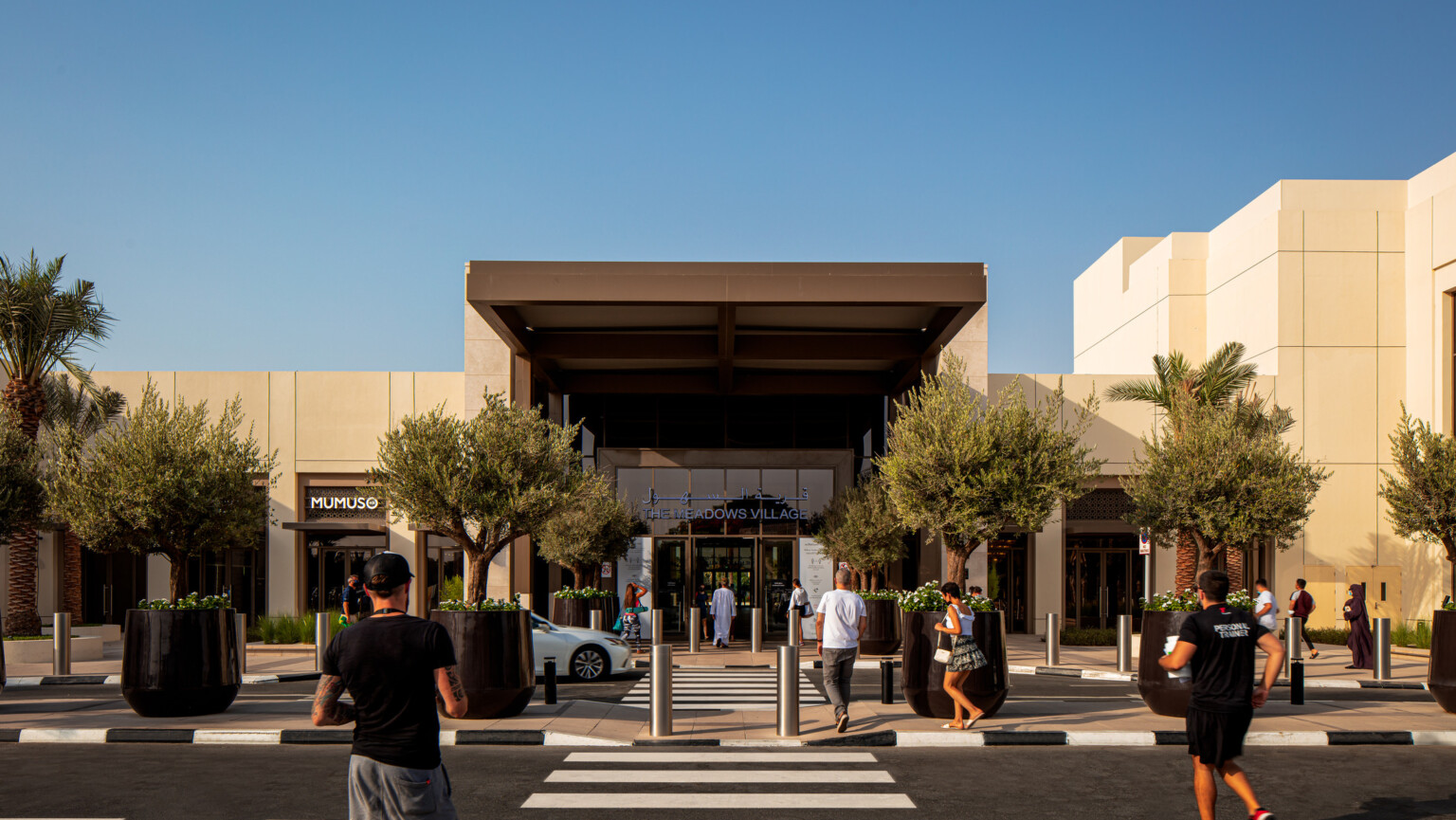 Pedestrians stroll toward a vibrant shopping center showcasing a variety of stores and a lively atmosphere.