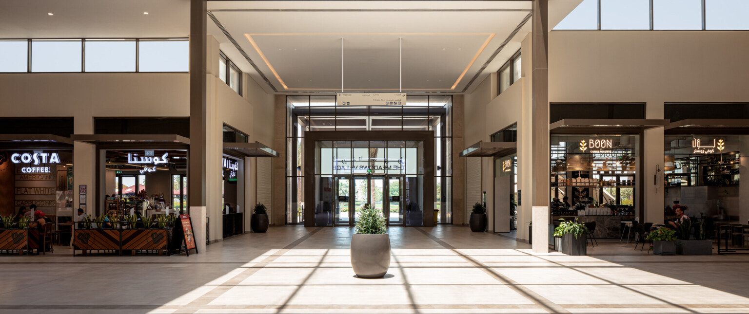 Interior of a shopping mall with lots of natural light beaming down onto a plant in front of several storefronts