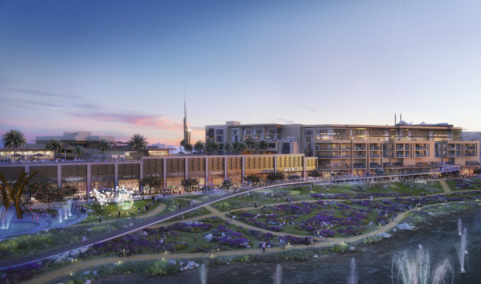 Midrise shops and buildings line street across from garden with purple flowers and multiple fountains with view of city