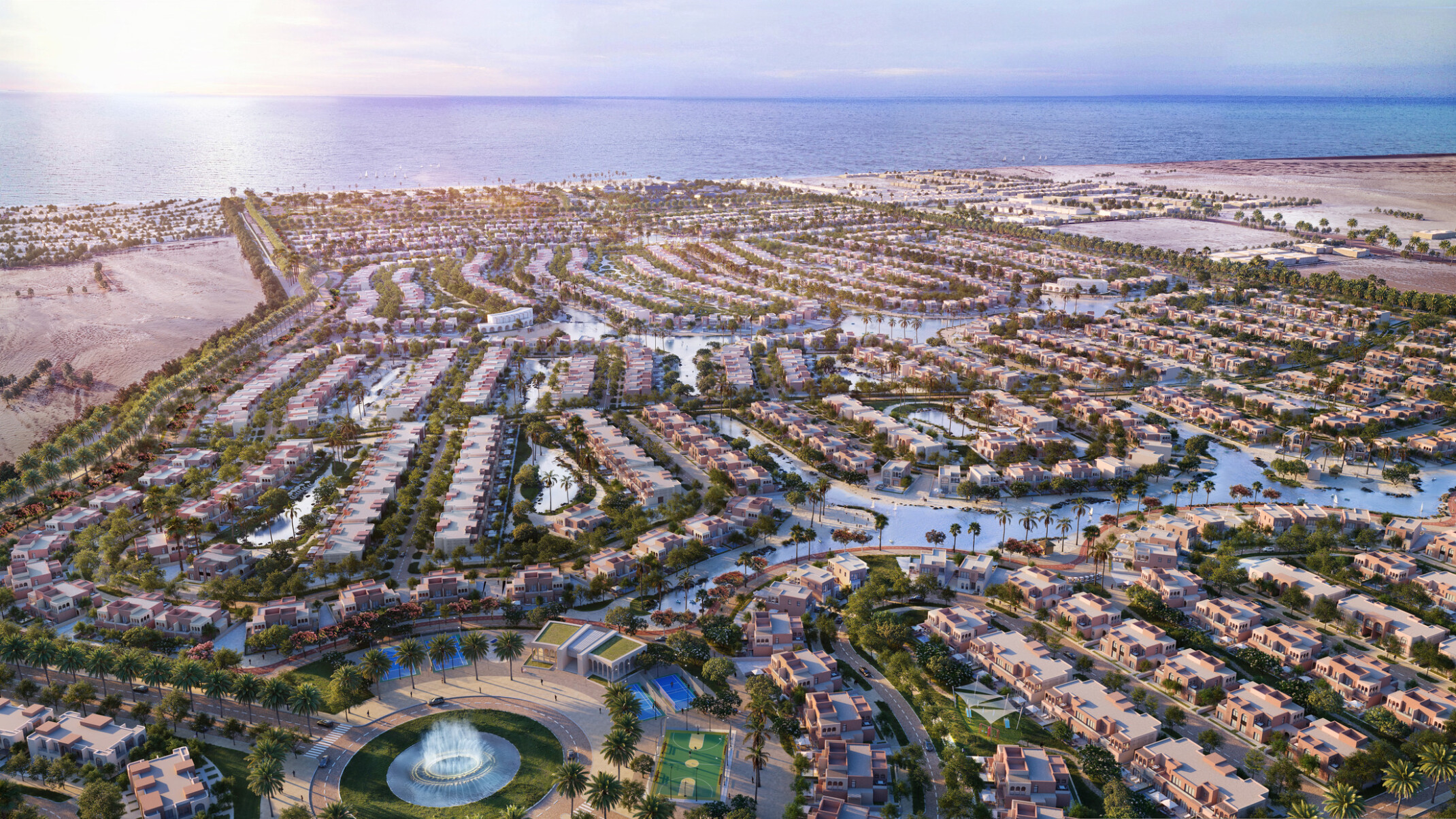 aerial view of a modern community with winding pathways and greenery throughout; the community overlooks the ocean and integrates water in the neighborhood rows