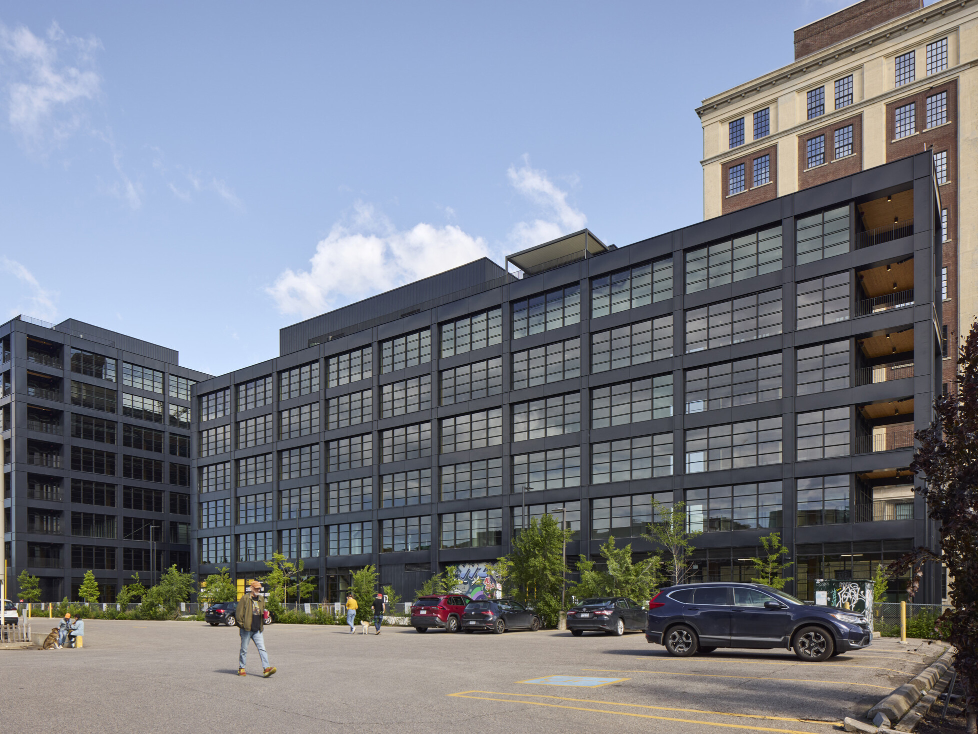 Black multistory office building filled with windows in front of a larger multistory office building