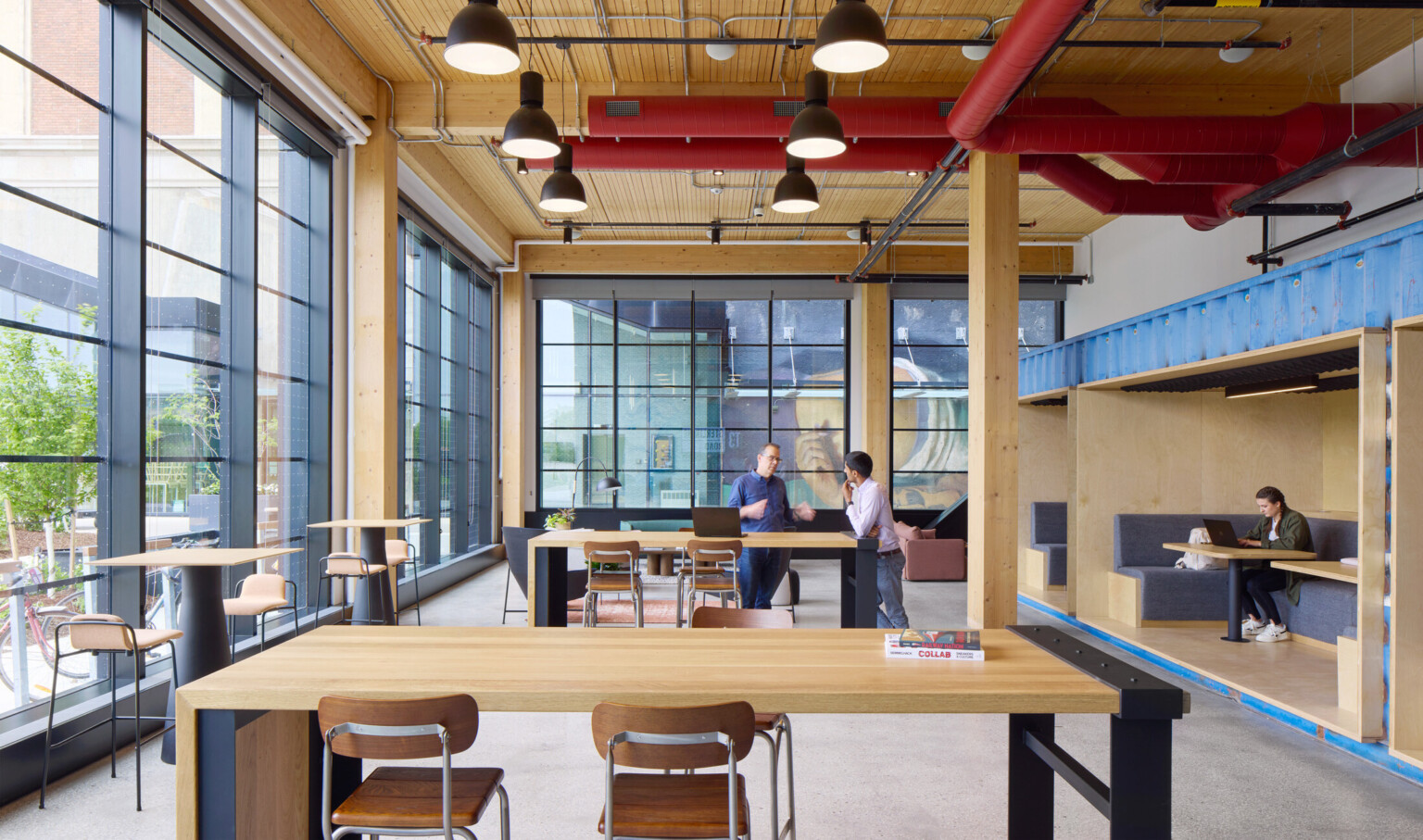 Large office space with exposed wooden beams, large black framed floor to ceiling windows, filled with multiple seating areas