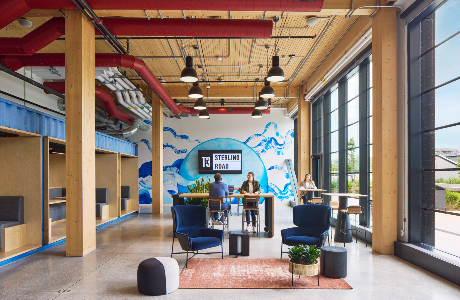 interior design of a mass timber building in toronto; two people working at a high top table with a large mural wall in the back; dlr group design interior design of a mass timber building in toronto; two people working at a high top table with a large mural wall in the back; dlr group design