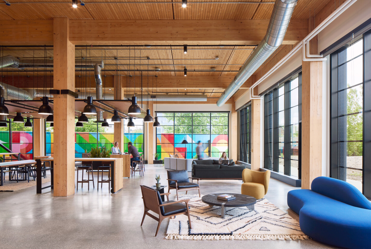 Large office space with exposed wooden beams, floor to ceiling black framed windows, and colorful mural outside