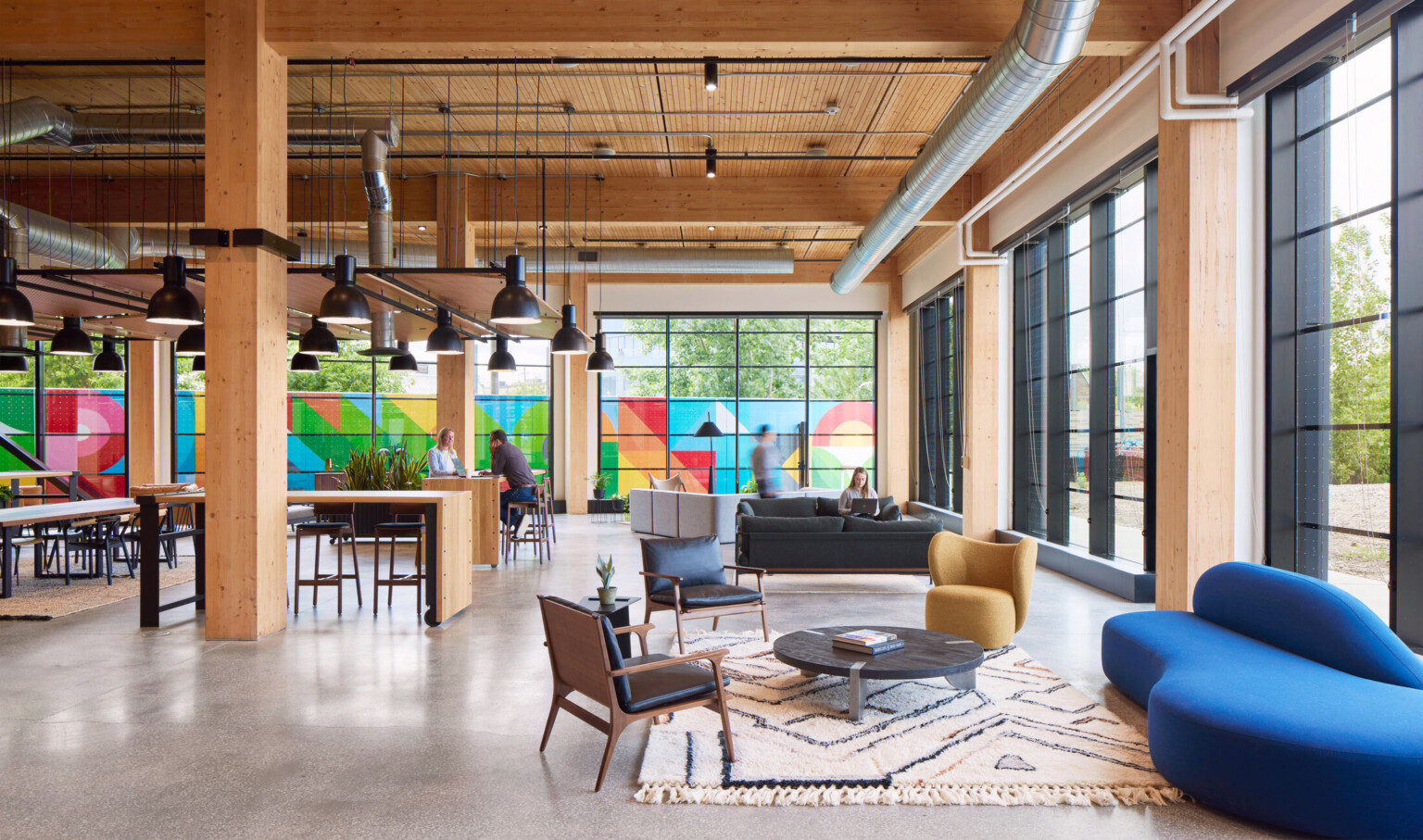 Large office space with exposed wooden beams, floor to ceiling black framed windows, and colorful mural outside