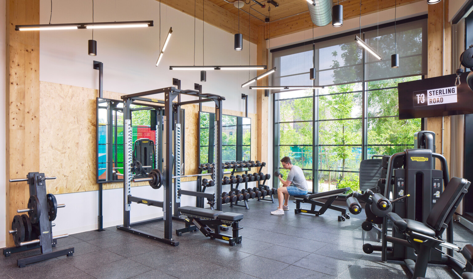 Indoor gym filled with exercise equipment, large black framed floor to ceiling windows and wooden accents throughout
