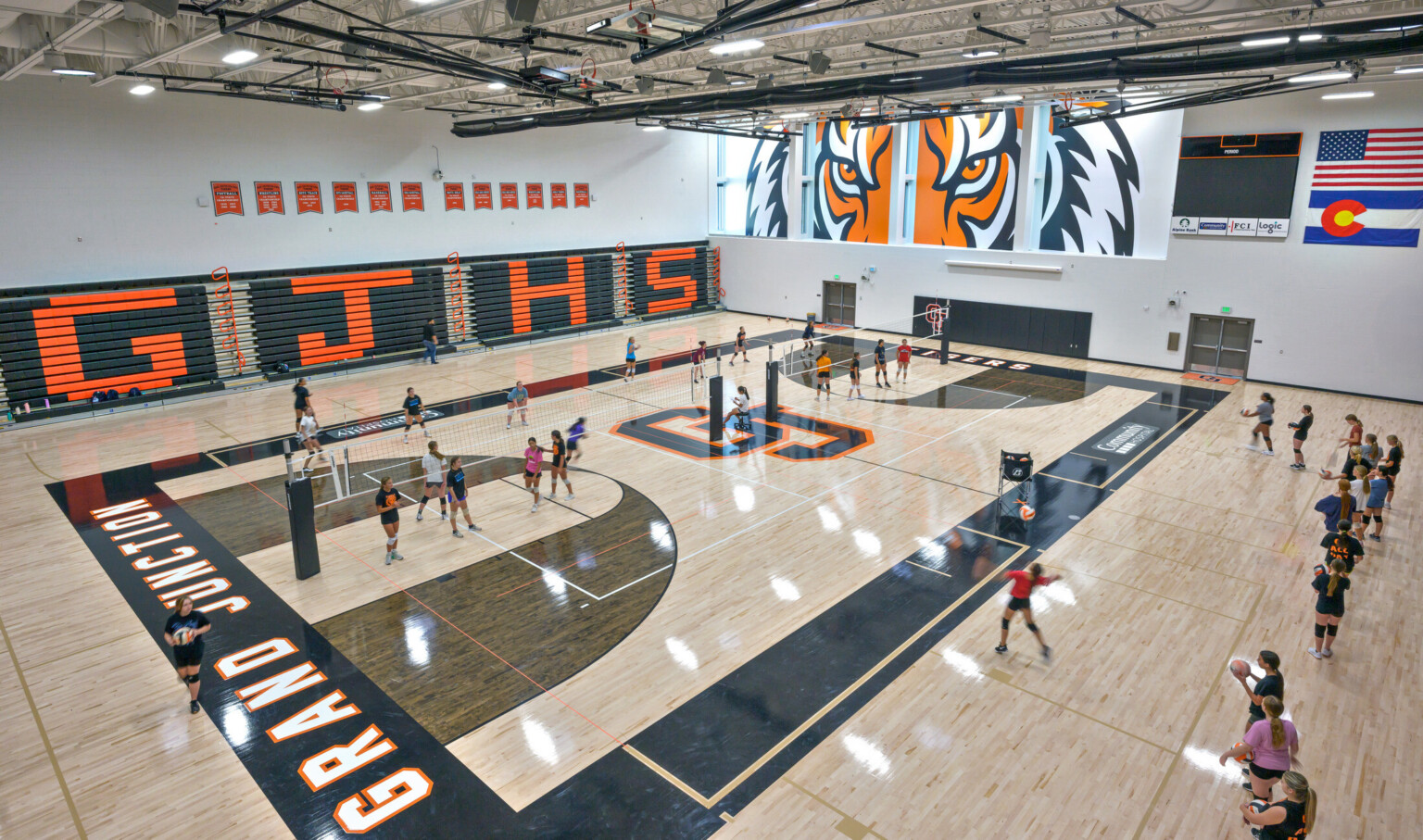 large elevated shot of high school volleyball practice; Grand Junction logo, orange and navy blue colors decorate the court; close up animated image of a tiger