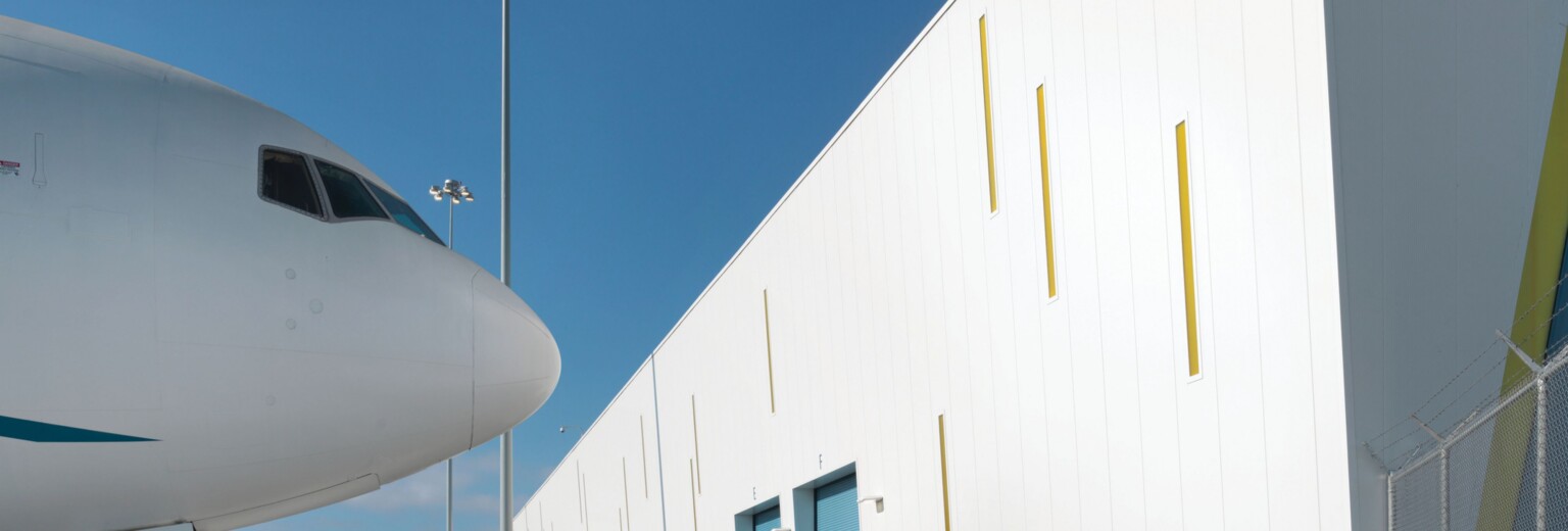 nose of an airplane against a blue sky; next to a white building
