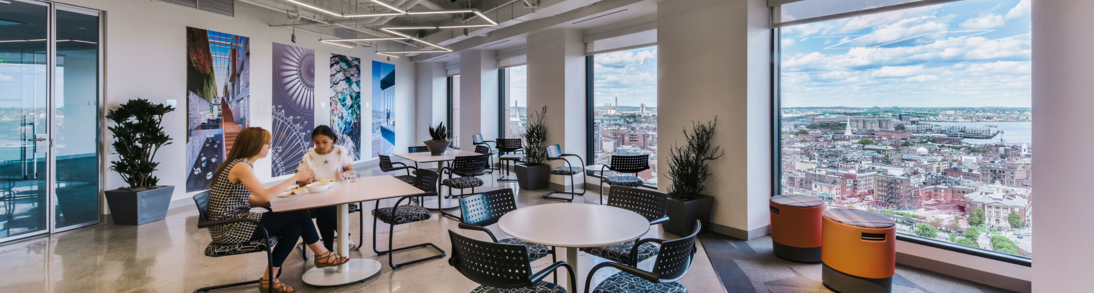 modern office collaboration hub with varied seating and people working at tables in front of floor to ceiling windows; DLR Group Boston office