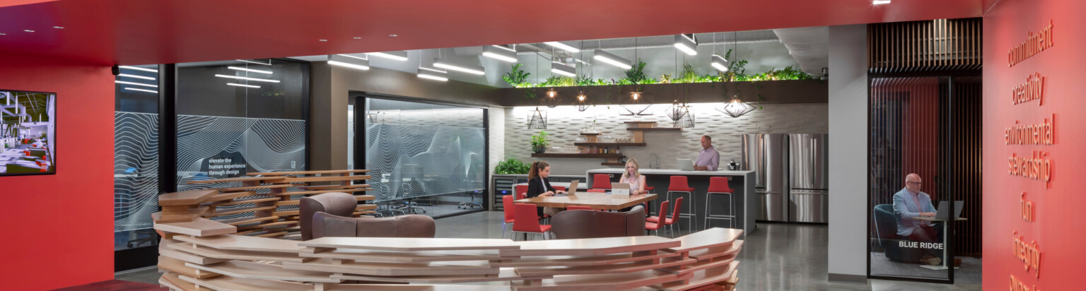 modern office front entrance desk with community collaboration space in the background; front desk surrounded by red walls and carpeting; DLR Group Charlotte office