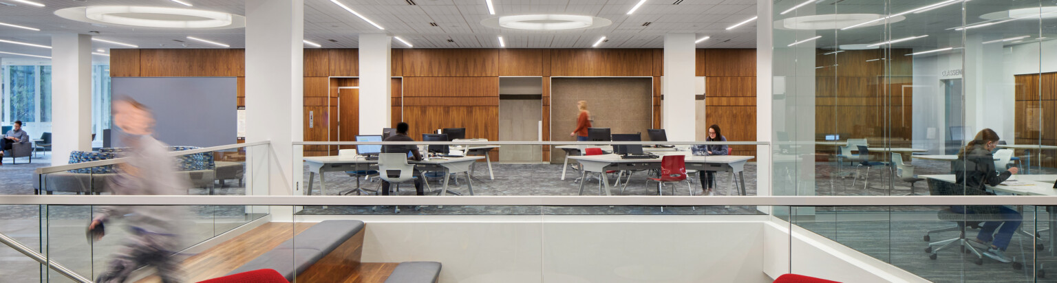 modern bright library space with central descending staircase; people at tables working