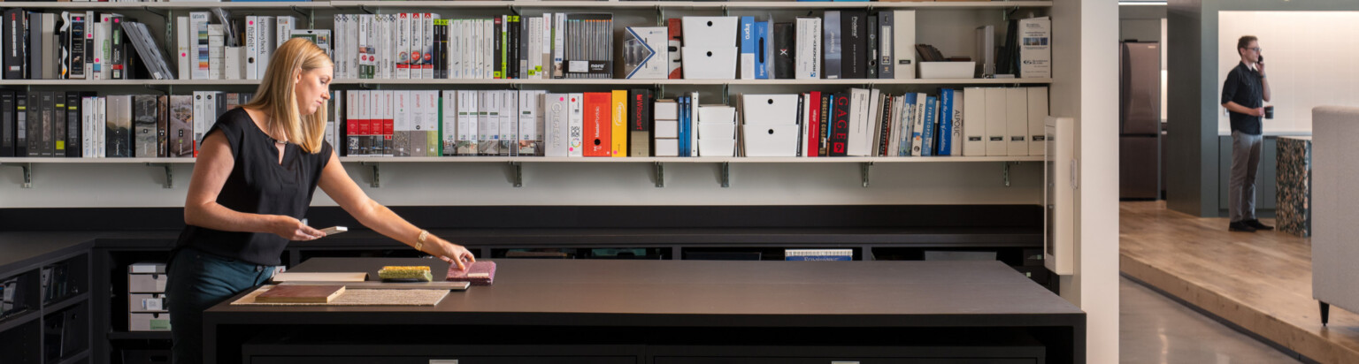 woman standing in a interiors material library at a high top table; DLR Group Orlando office