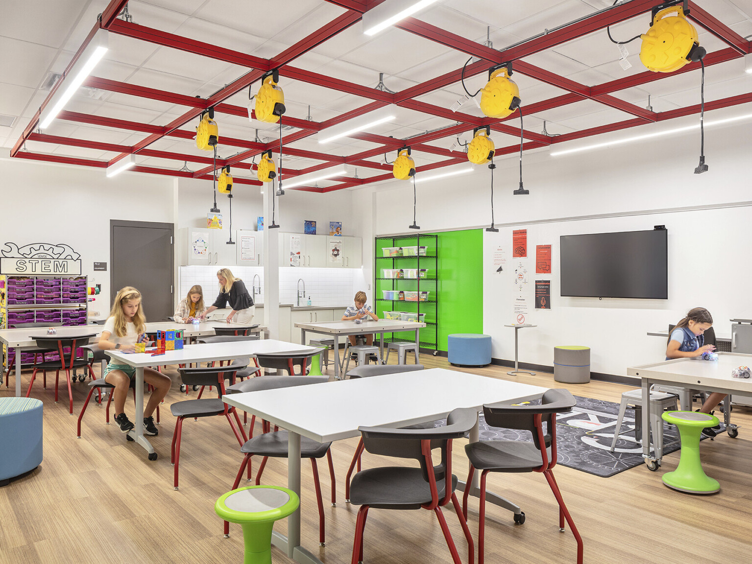 Modern STEM classroom filled with tables, and chairs. Students engaged in activities around the room, yellow plugs suspended from the ceiling