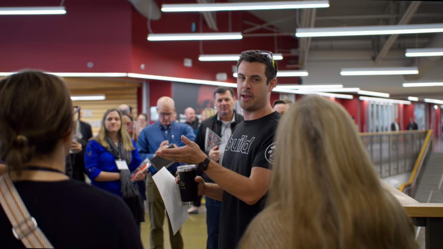 Group of people assembled around a man in a black shirt expressively speaking to the crowd.