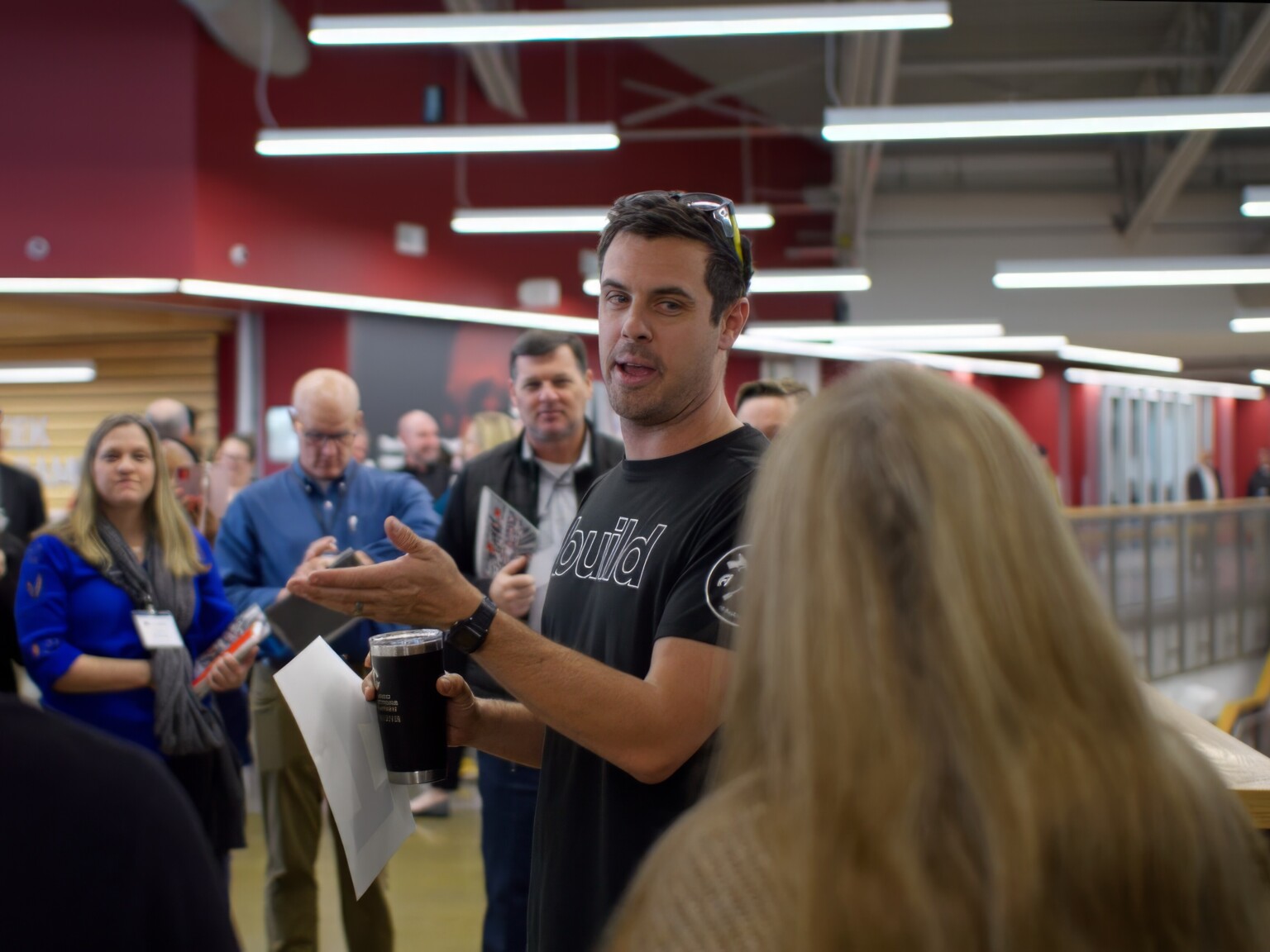 Group of people assembled around a man in a black shirt expressively speaking to the crowd.