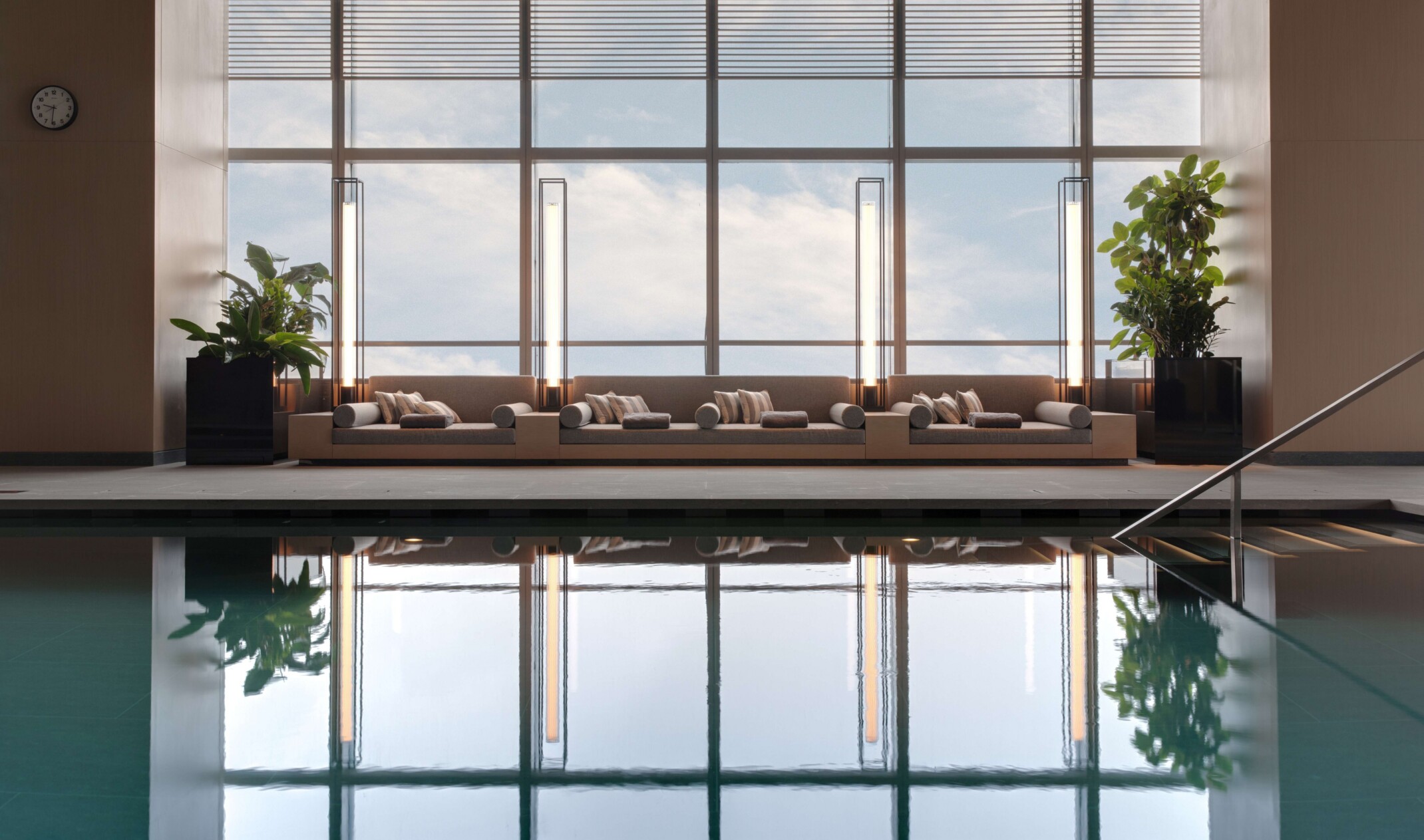 Luxury swimming pool room in front of tan lounging pool furniture overlooking floor to ceiling windows
