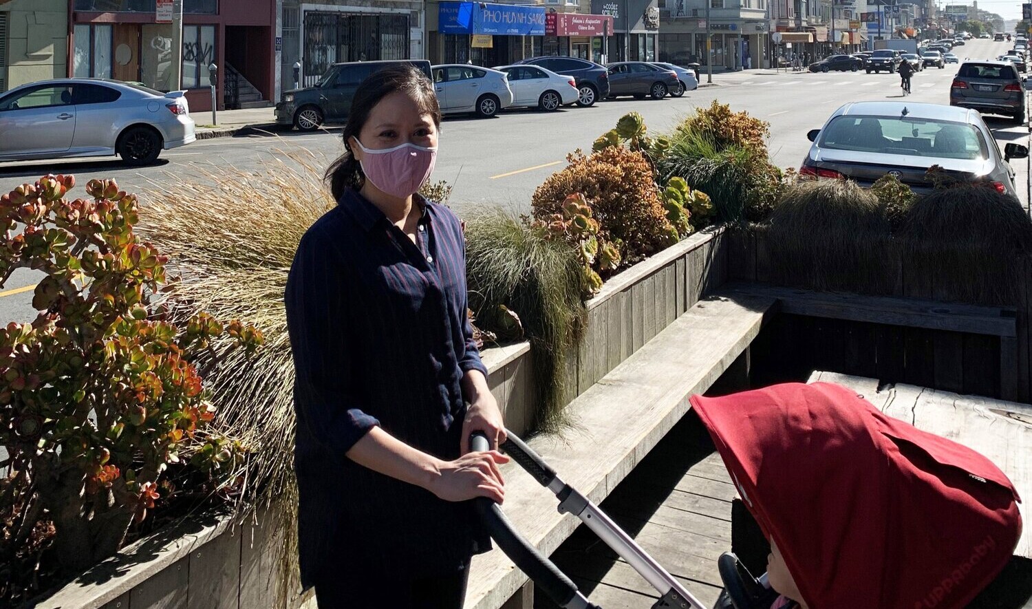 Catherine Meng pushing a red hooded stroller in an outdoor seating area on a street with row buidlings Catherine Meng pushing a red hooded stroller in an outdoor seating area on a street with row buidlings
