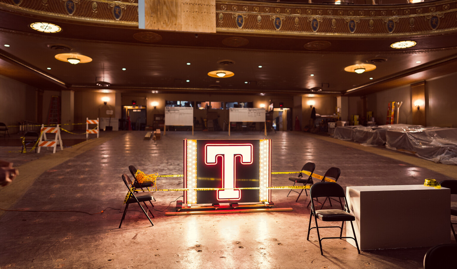 Illuminated letter T in box with lights on sides inside of partially constructed theater with no seats, molding on balcony Illuminated letter T in box with lights on sides inside of partially constructed theater with no seats, molding on balcony