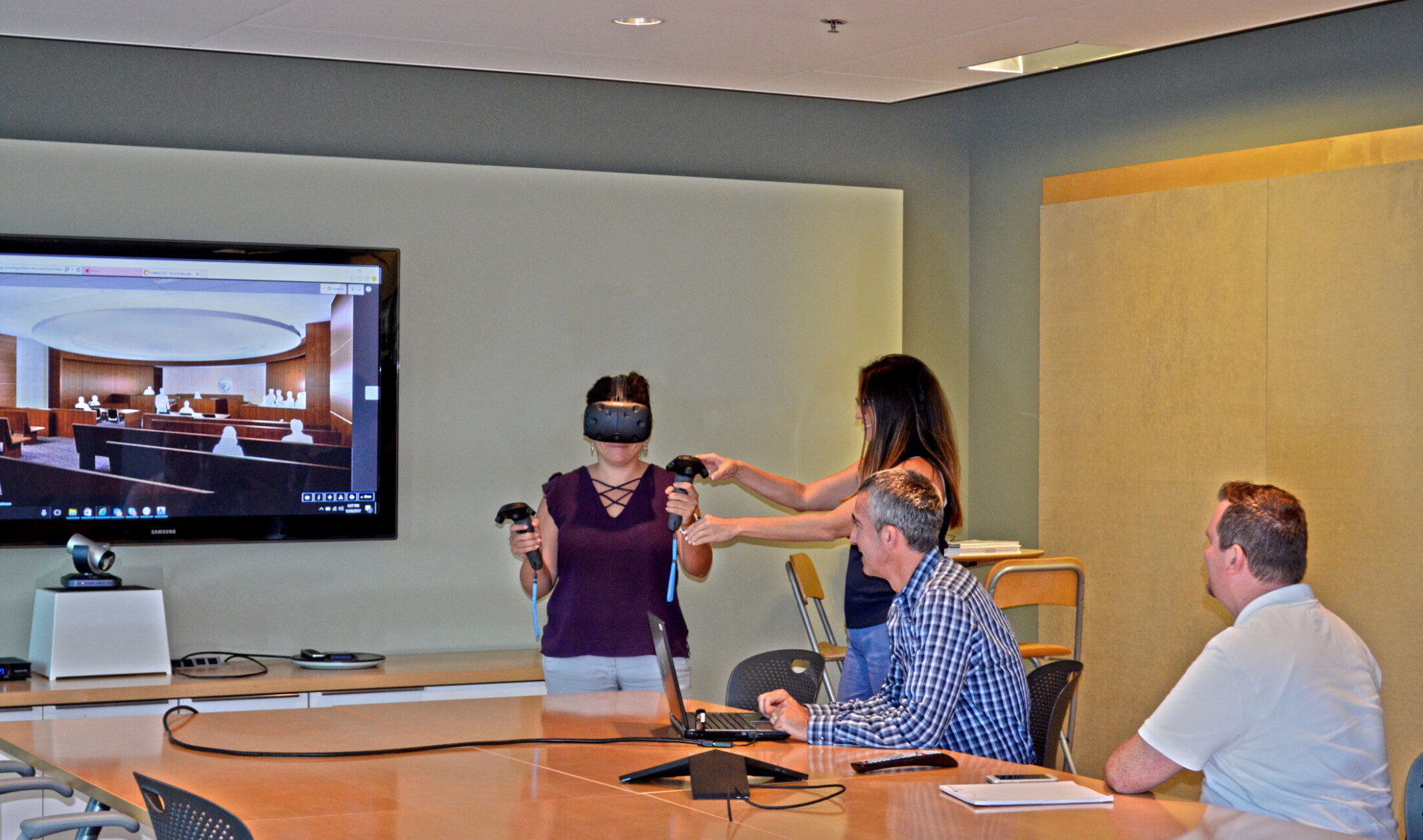 people around a table where woman is using virtual reality system to experience mock-up of courtroom design