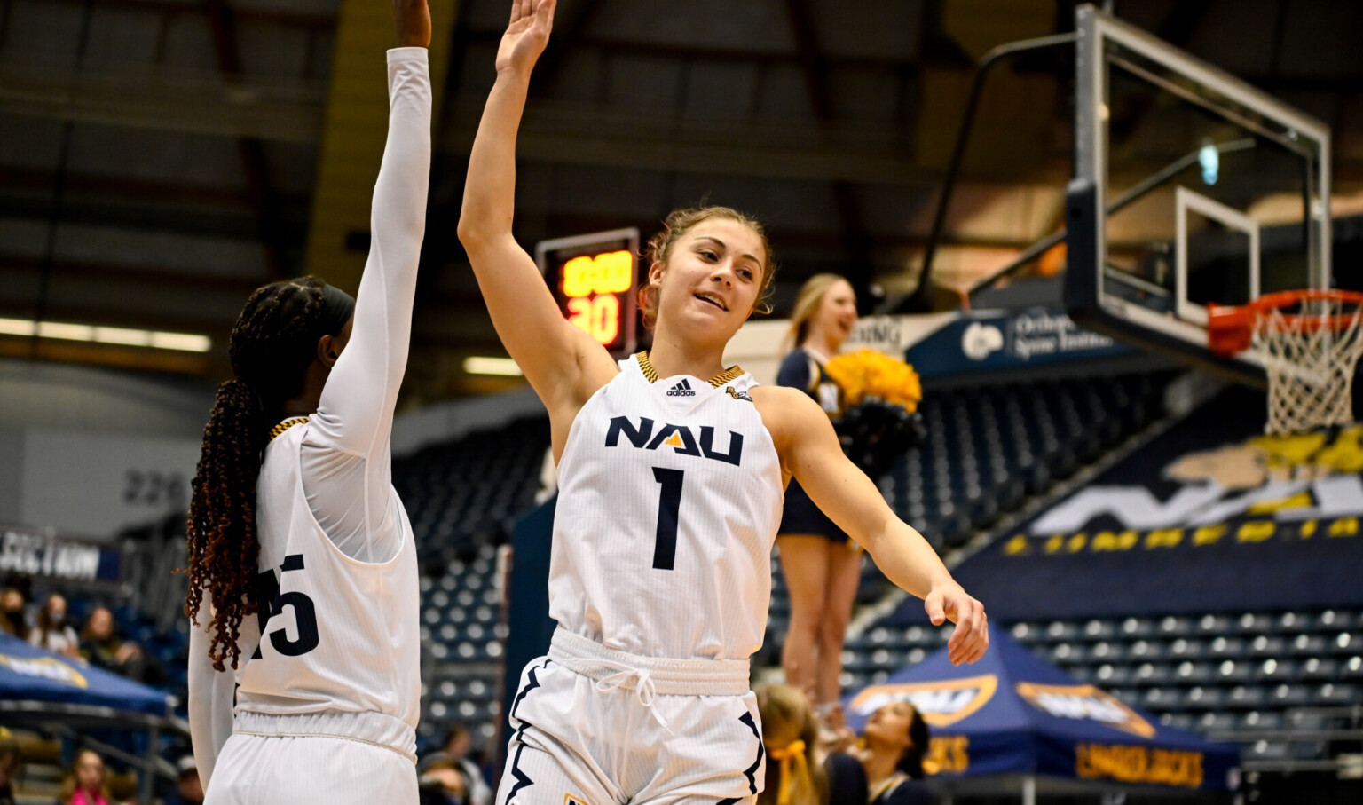 Northern Arizona University female student athlete high fiving during basketball game on court basket upper right Northern Arizona University female student athlete high fiving during basketball game on court basket upper right