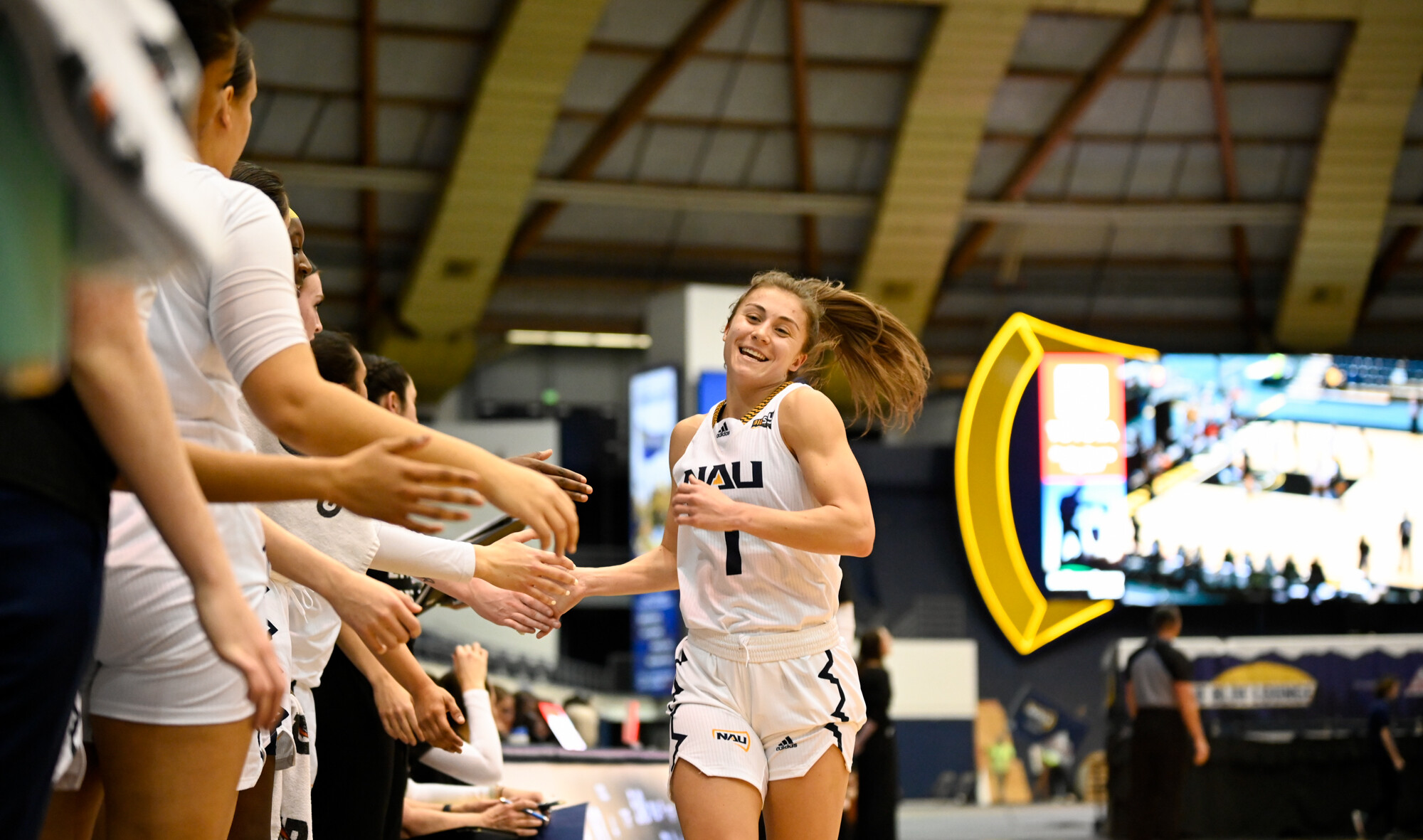 a female basketball player in a Northern Arizona Uniform white uniform in a crowded gymnasium filled with cheering fans