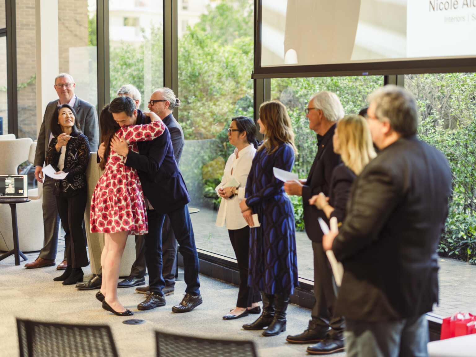 Newly appointed employee-owner is recognized and hugs a line of firm principals at office 2024 appointment party