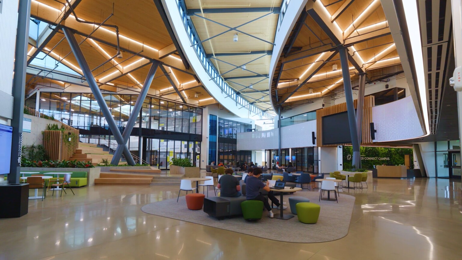 interior of a modern building with exposed beams and architectural structures; students working at modular desks in the center of the double height space